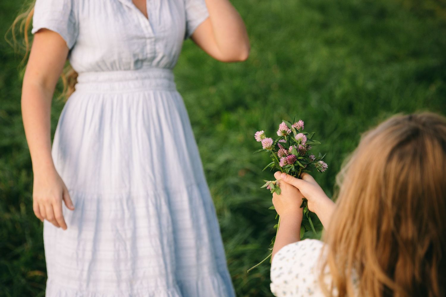 A group in white dresses gathers outdoors for a summer celebration in a lush green garden setting.