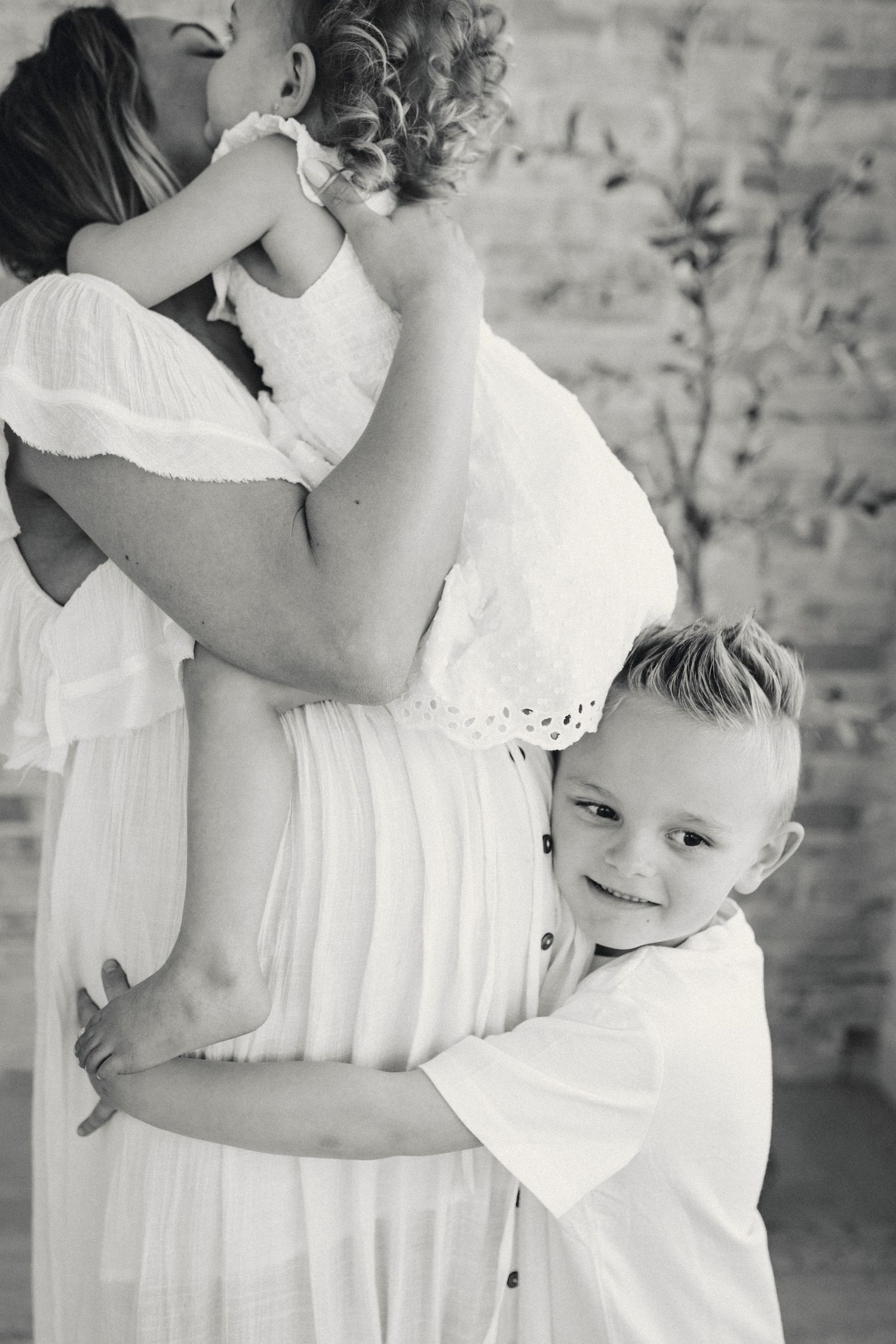 Black and white portrait of embracing family with child hugging pregnant belly.