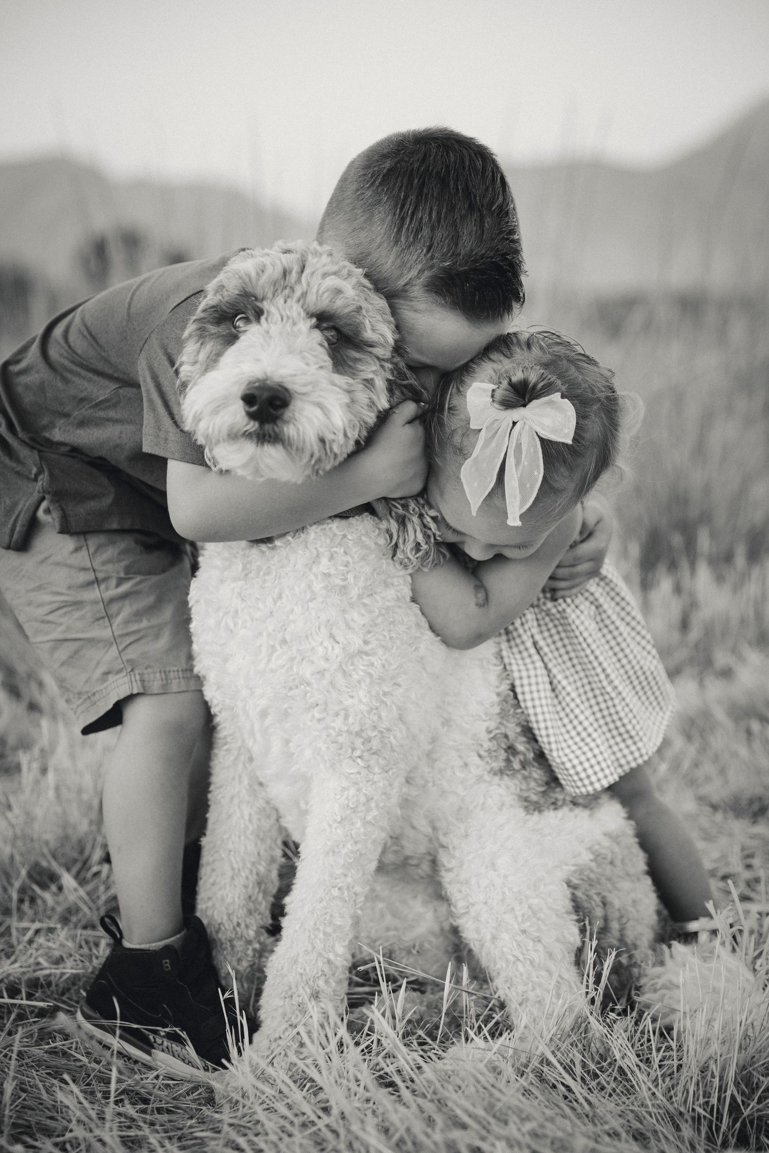 Child hugs fluffy white dog in black and white portrait outdoors.