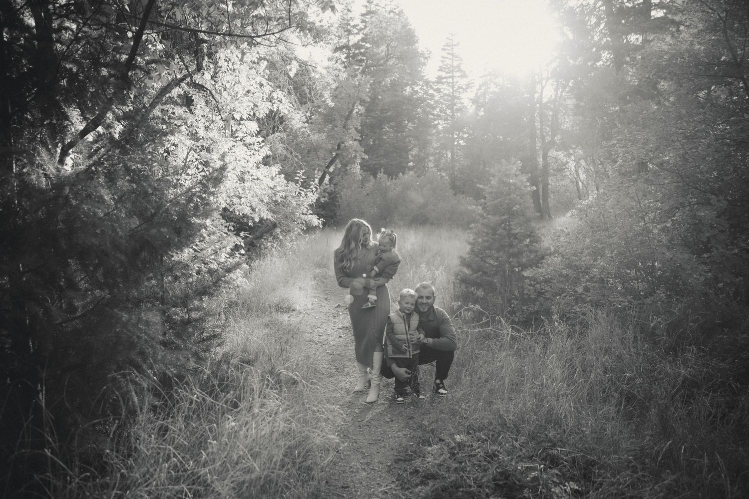 A black and white photograph of people walking on a misty forest path with sunlight filtering through the trees.