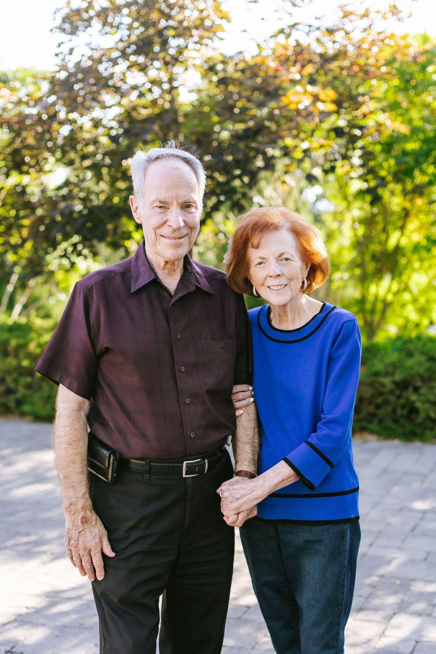 Two people in casual attire share an affectionate moment outdoors on a sunny day.