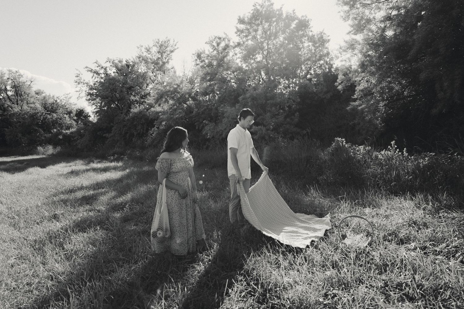 A couple shares a romantic moment in a sunlit meadow with tall grass and trees in the background.