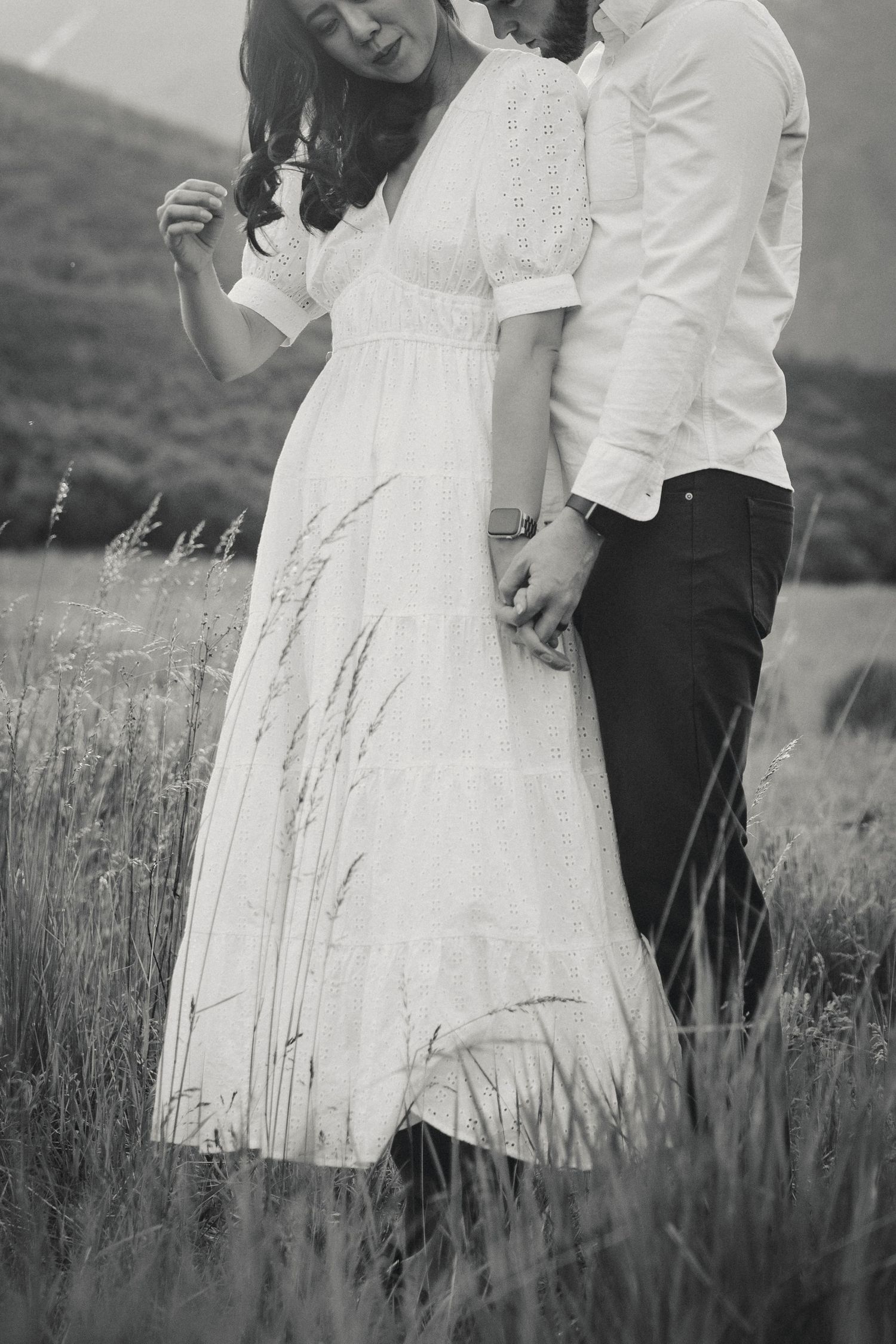Black and white photo of couple in formal wear standing in tall grass with vintage styling.