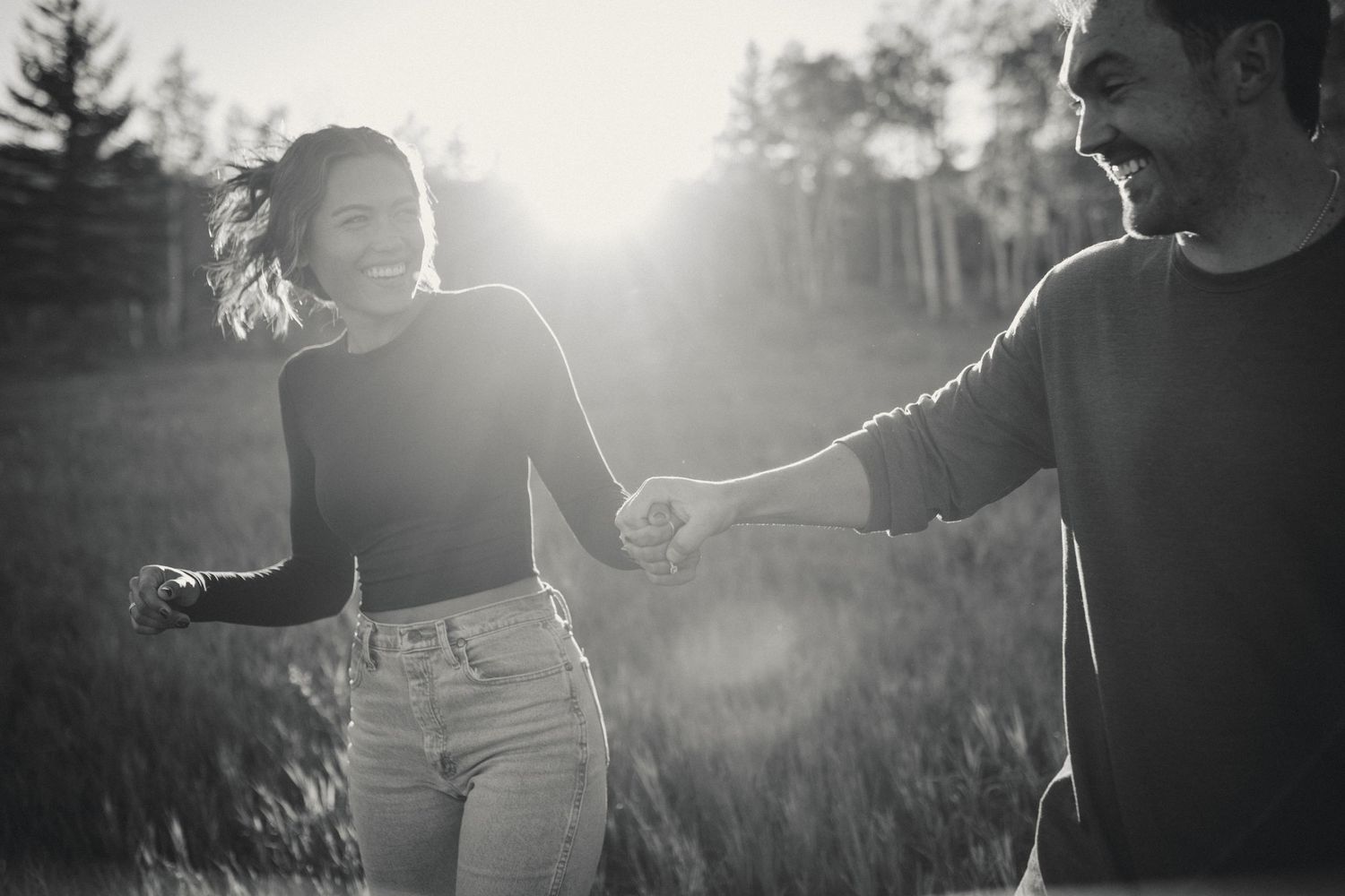 Couple holding hands in a sunlit field with dramatic lens flare creating a romantic silhouette.