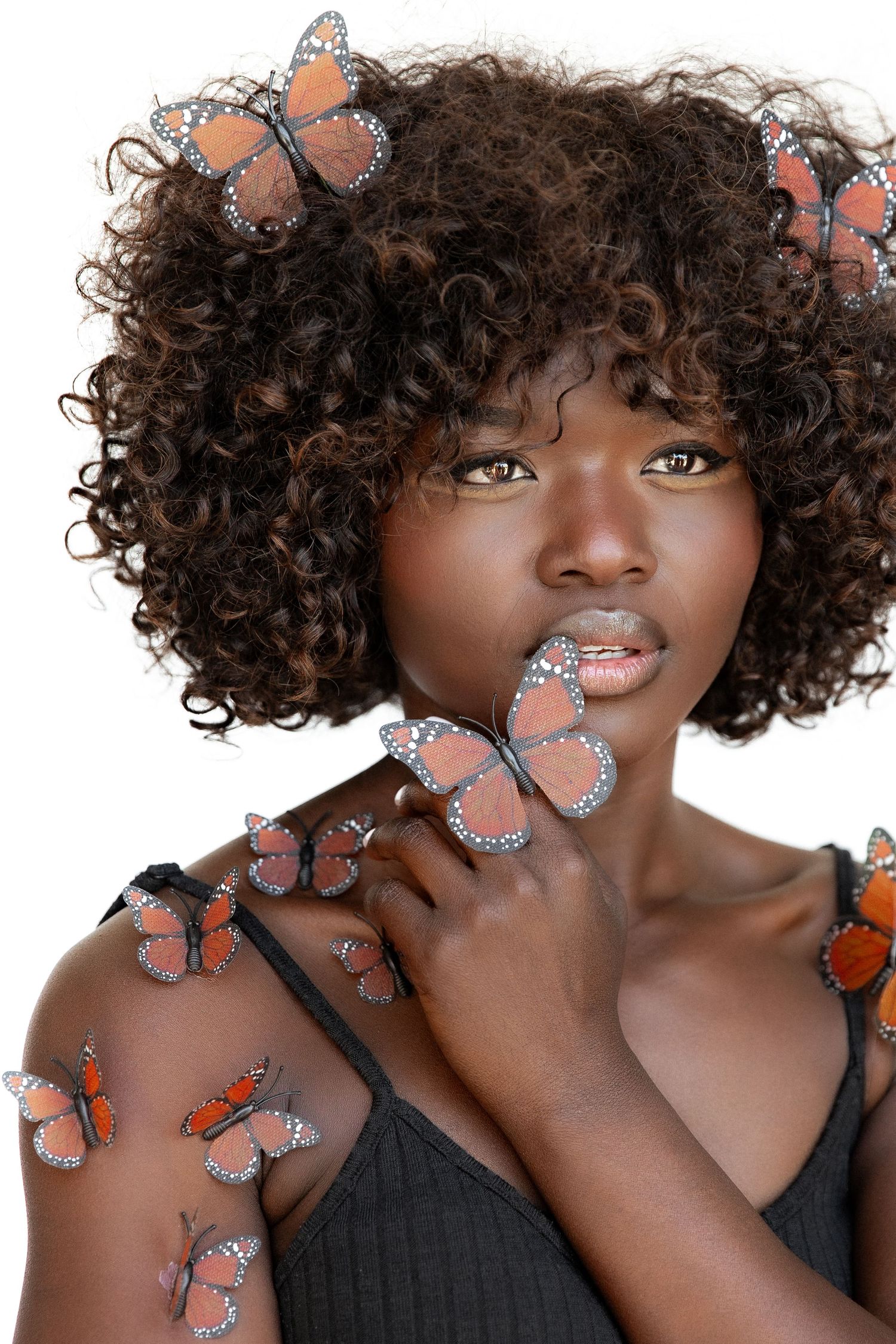 Creative portrait series with orange monarch butterflies against dark curly hair and black top.