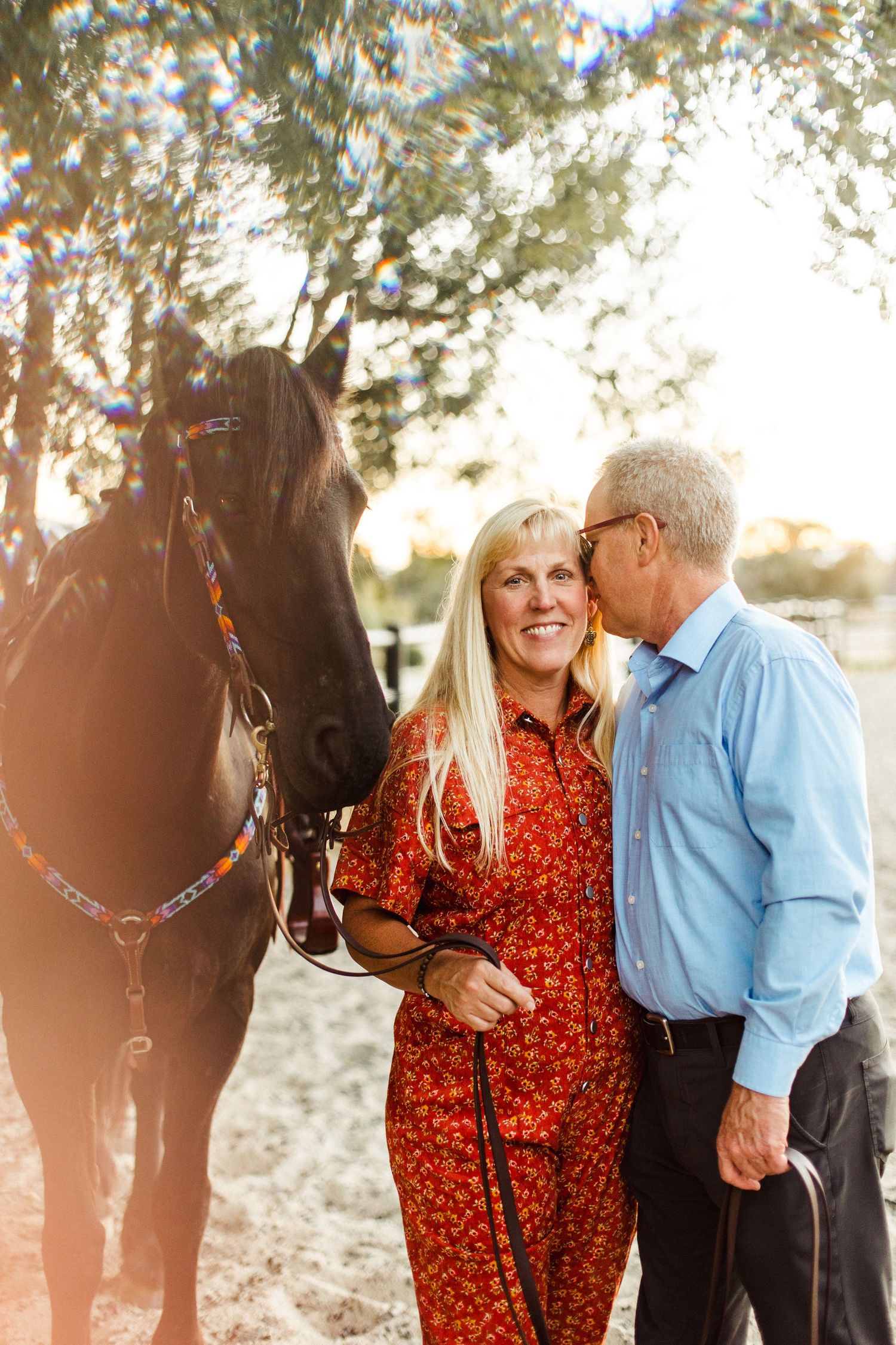A couple shares a moment with their beautiful black horse in warm sunlight.