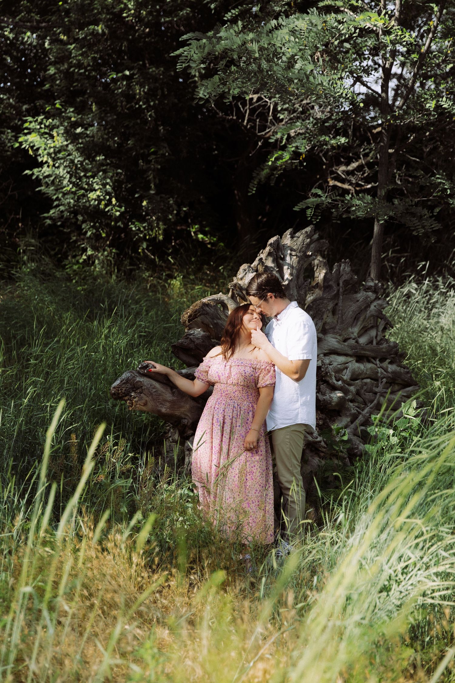 Couple sharing intimate moment among trees and rocks in lush garden setting.
