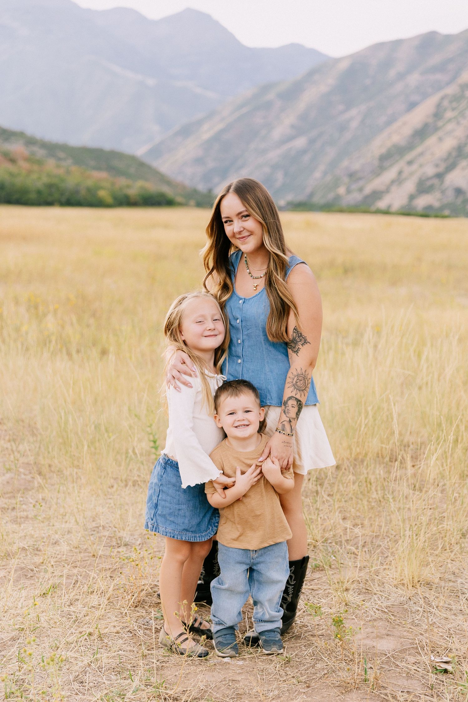 A parent and two children share joyful moments while posing in a mountain meadow.