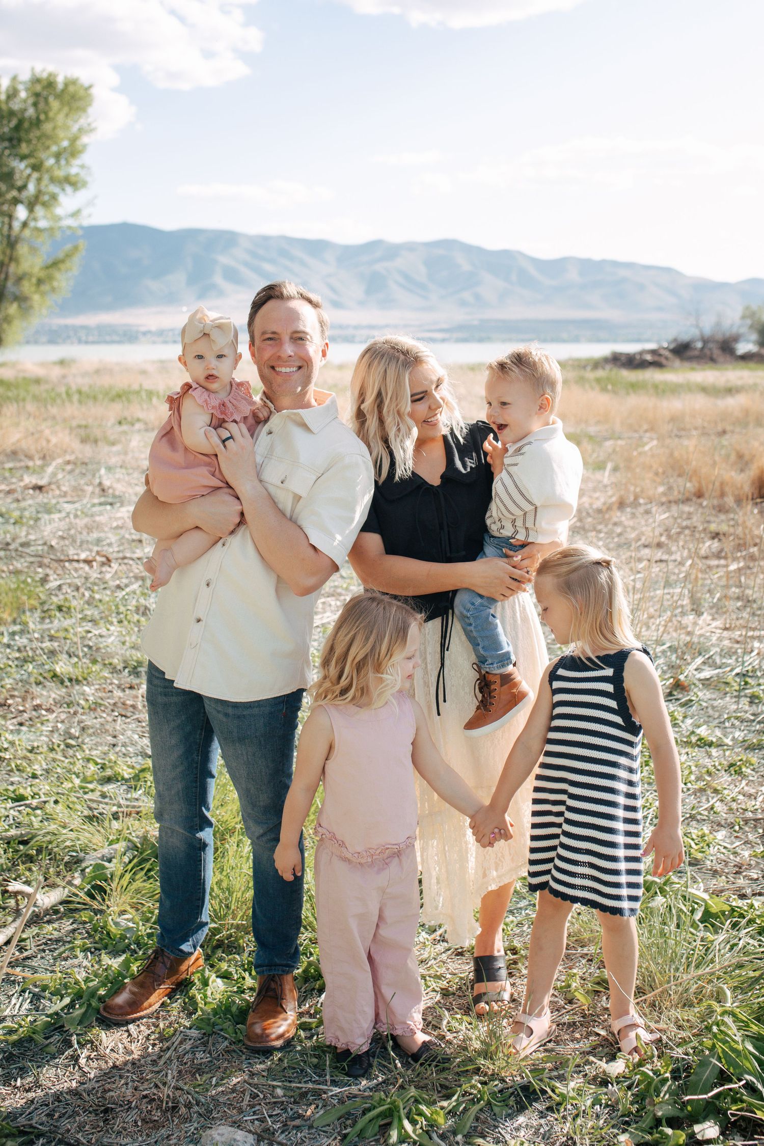 A family group shares joyful moments together in an outdoor setting with mountains and grassland in the background.