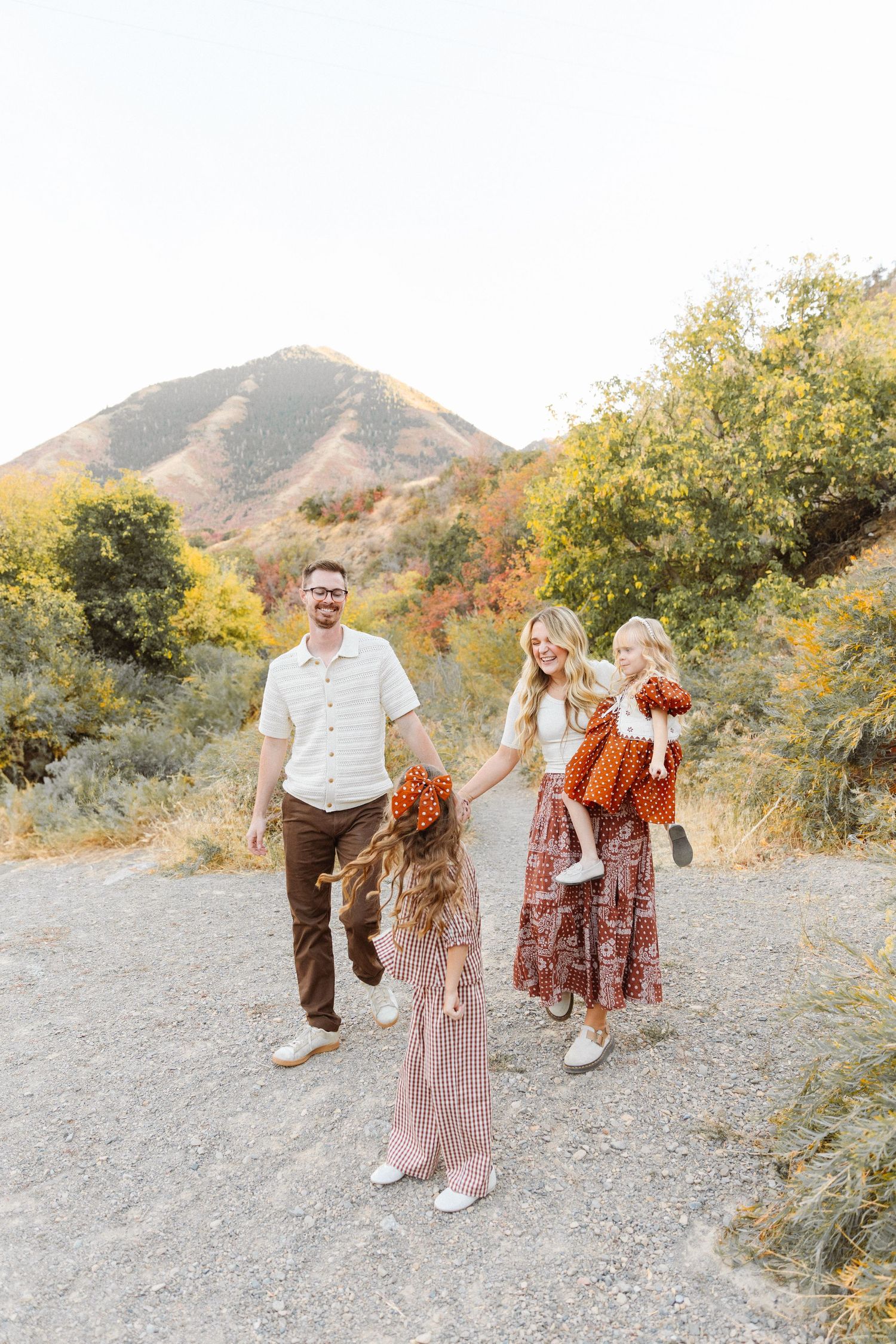Family walking together on desert trail with mountains and autumn foliage in background.