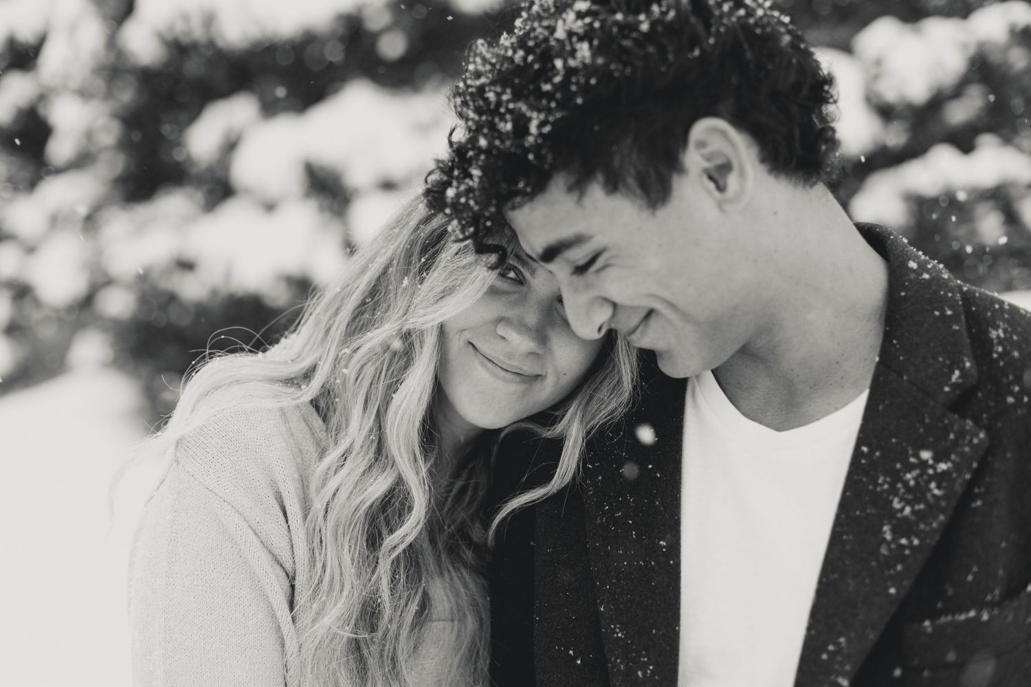 Two people share a close embrace during a snowy photoshoot in a winter setting.