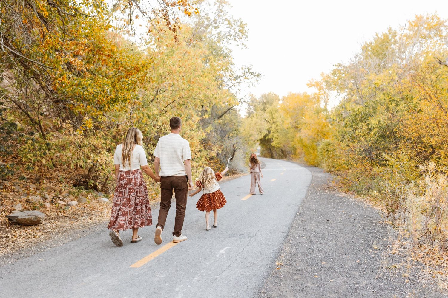 Family walking together on a dirt path surrounded by golden autumn trees.