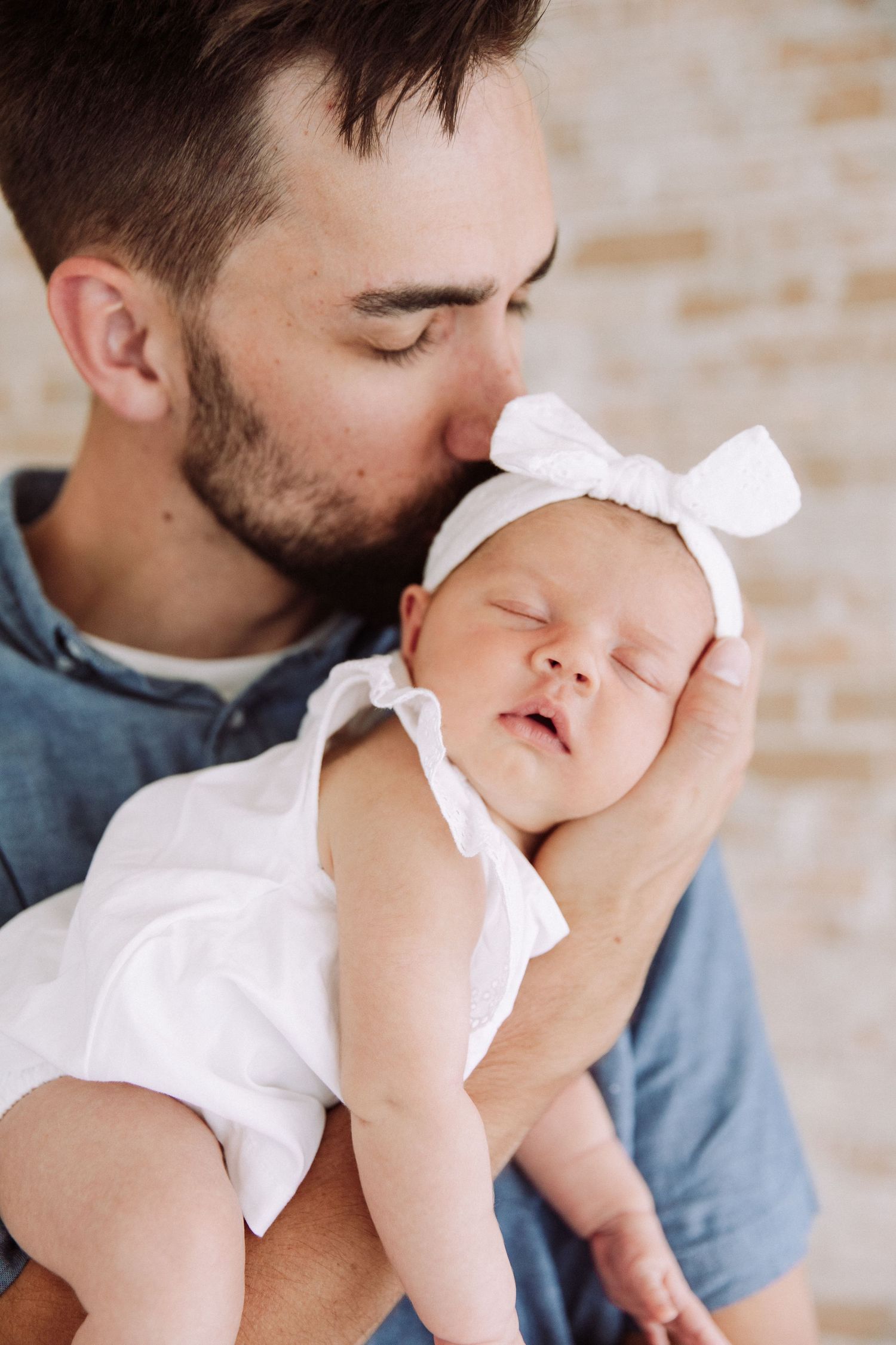Tender moments between parent and baby dressed in white against neutral background.