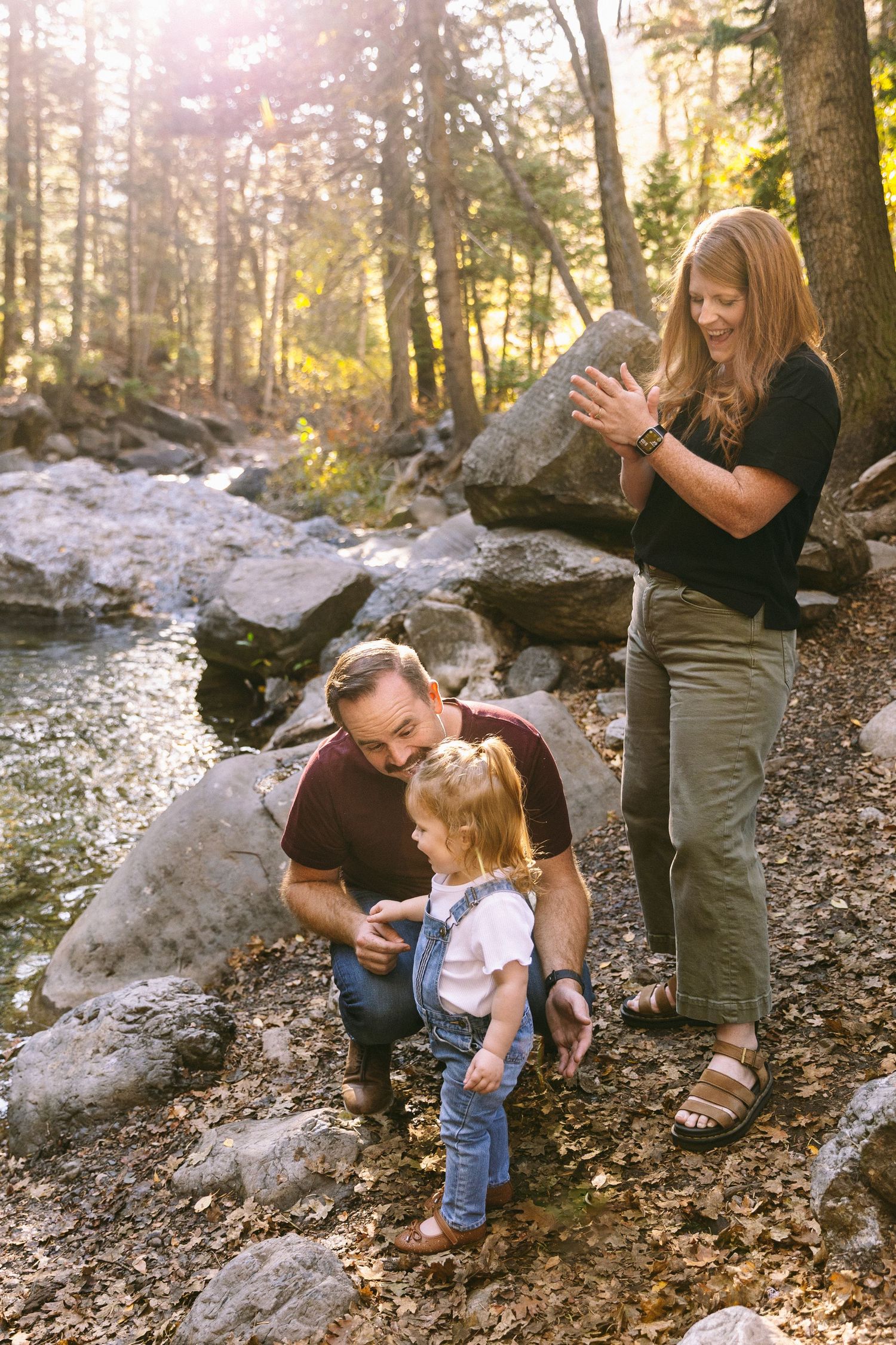 A family enjoys a peaceful moment together by a rocky stream in a sunlit autumn forest.