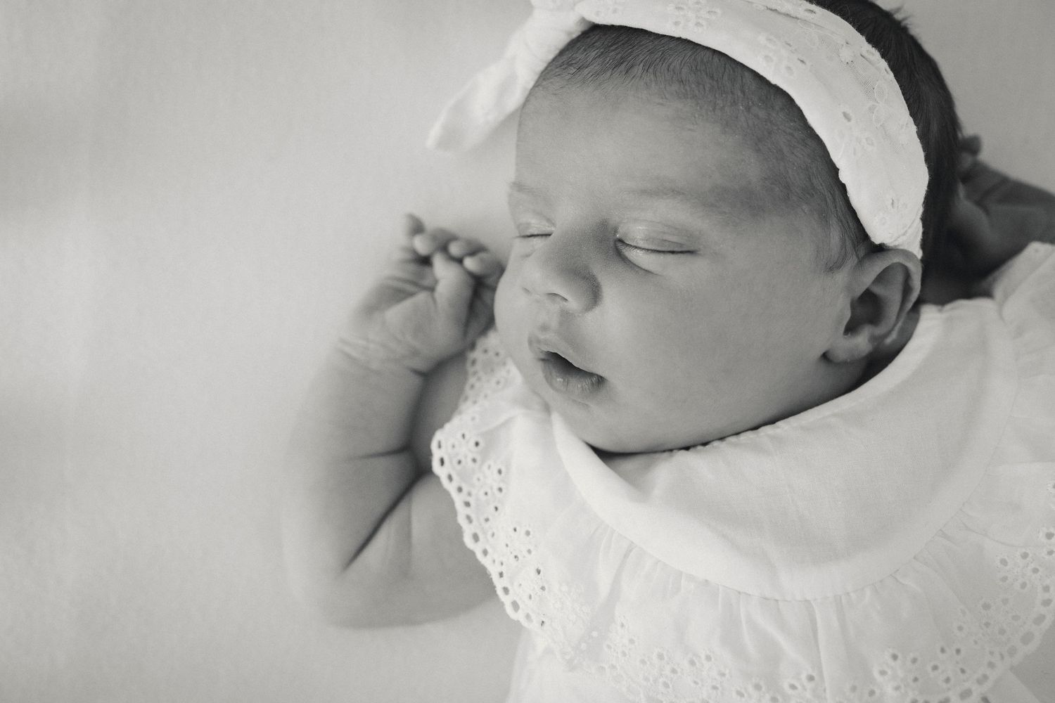 Peaceful sleeping baby wearing white lace clothing in soft monochrome tones.