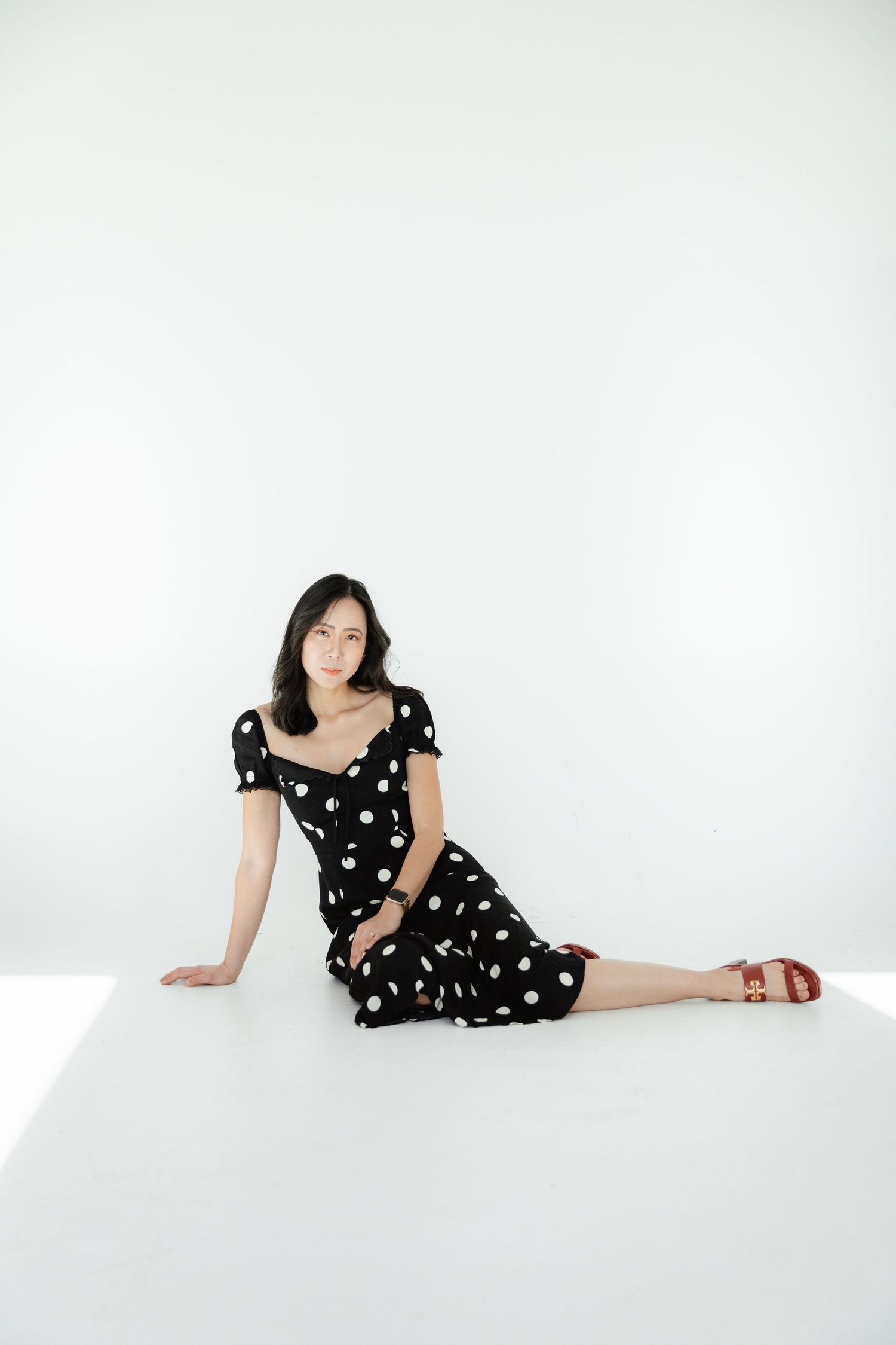 Woman in polka dot dress poses against white backdrop in studio setting.