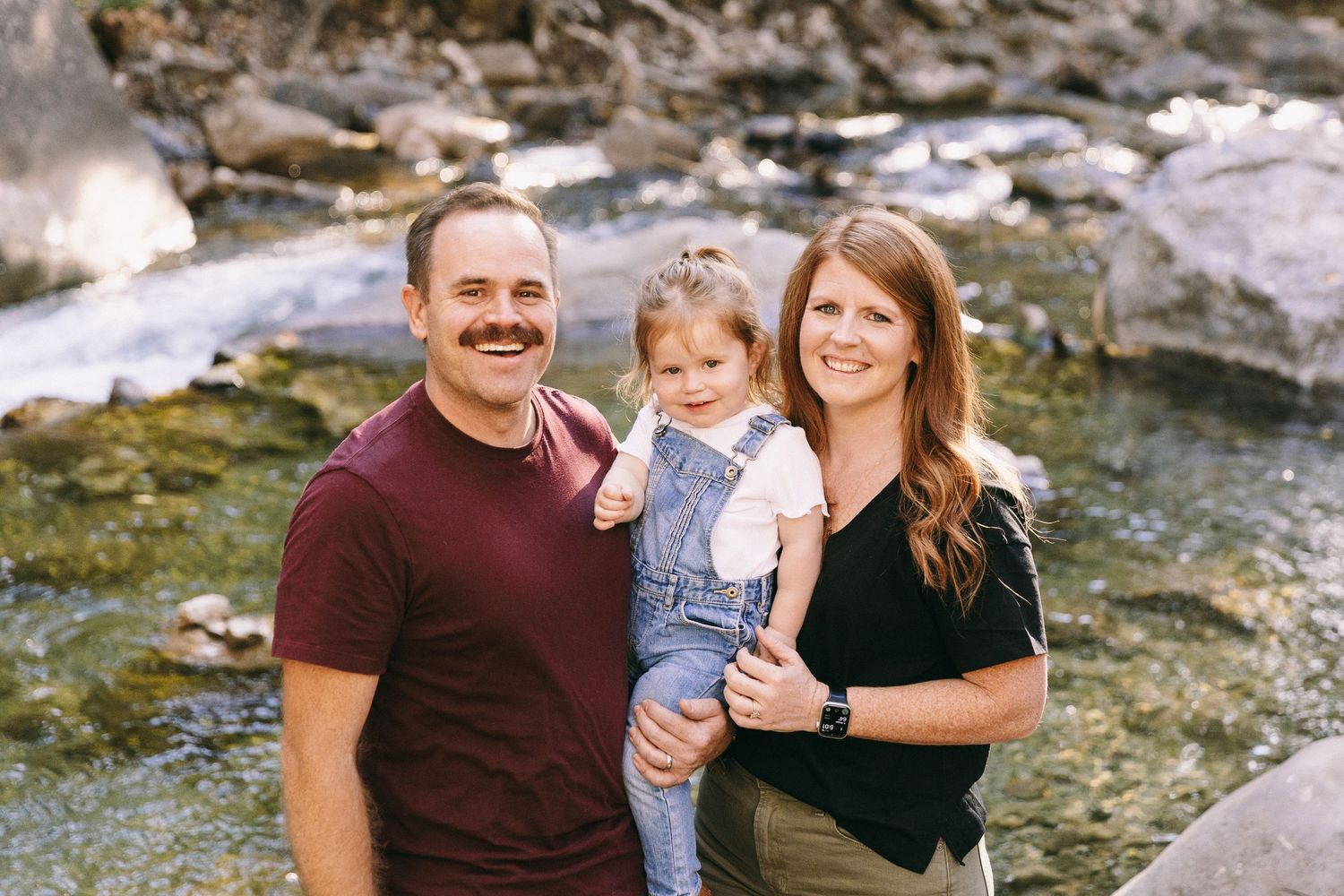 Family poses together near rocky stream during outdoor photo session in natural setting.