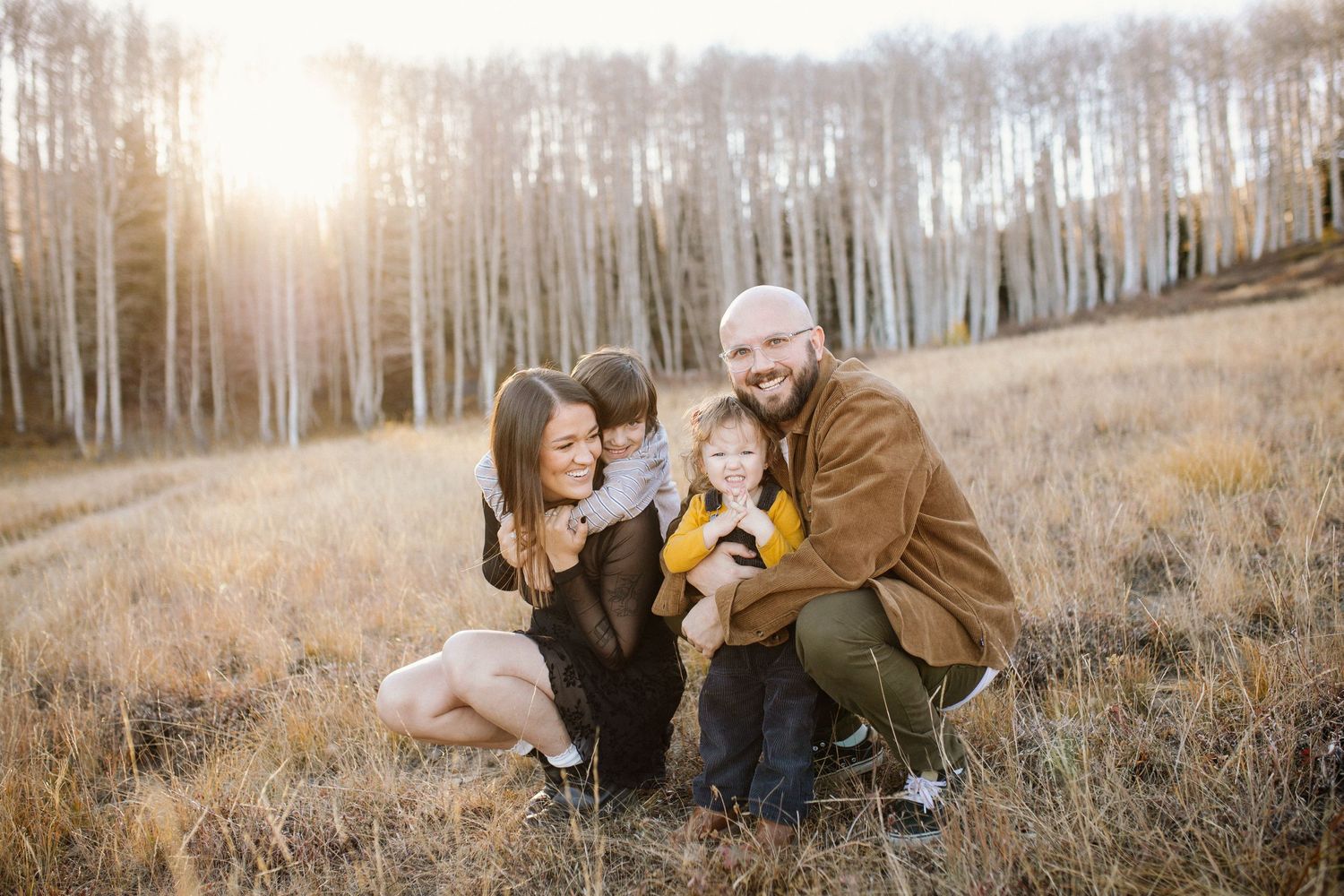 Family photo session in golden field surrounded by white aspen trees at sunset.