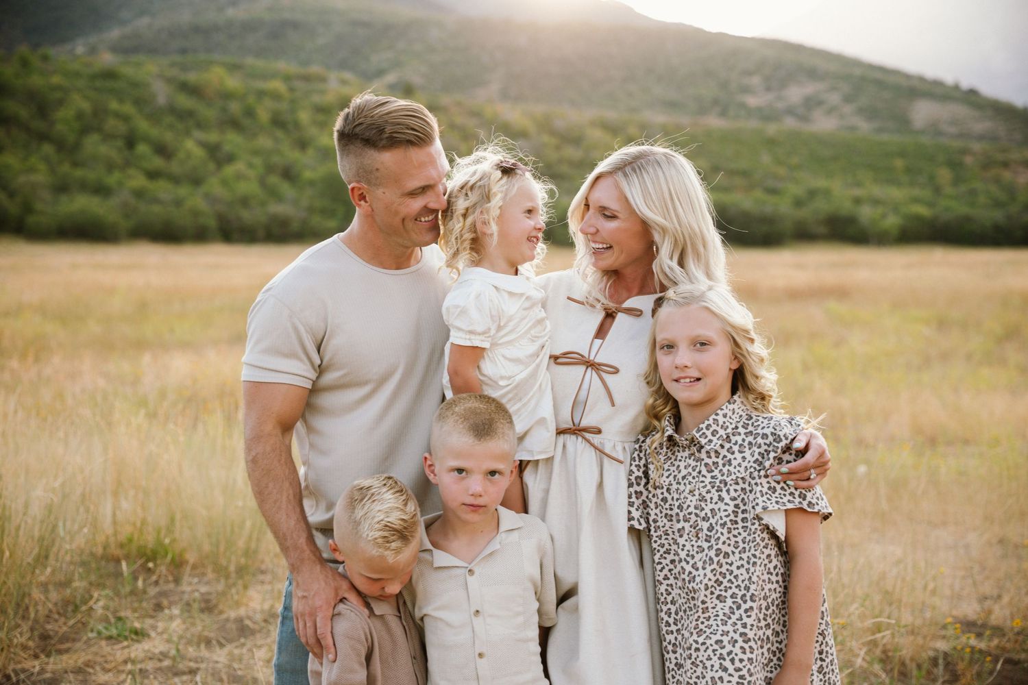 A group poses together in a golden field during sunset wearing coordinated neutral and white outfits.