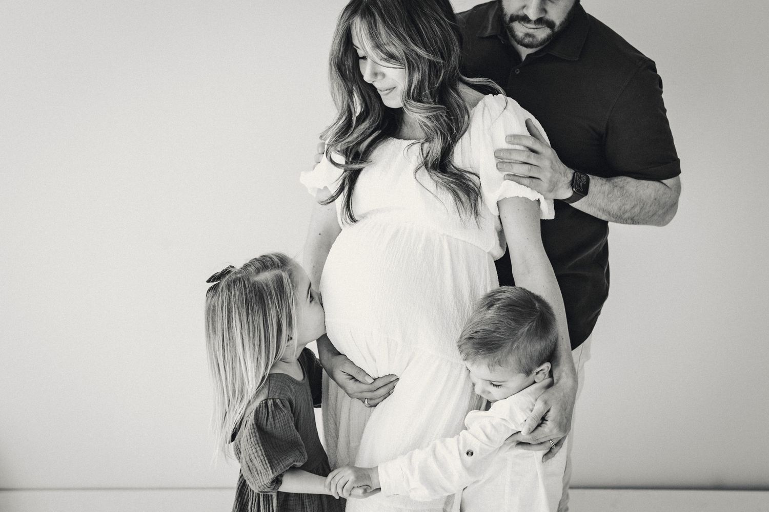 Black and white family maternity photo with children and parents embracing.