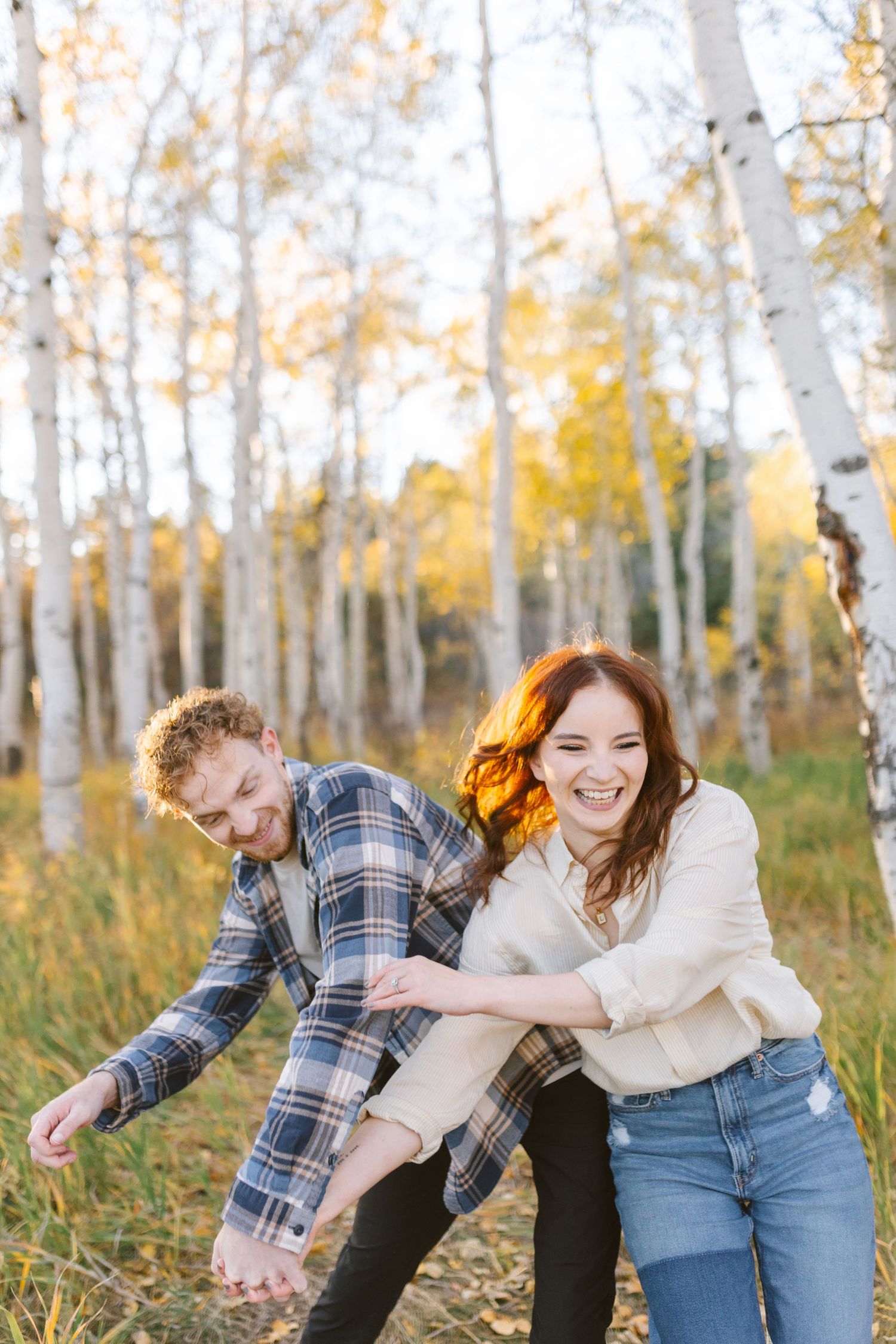 Couple playfully interacting in a grove of autumn aspen trees with golden leaves.