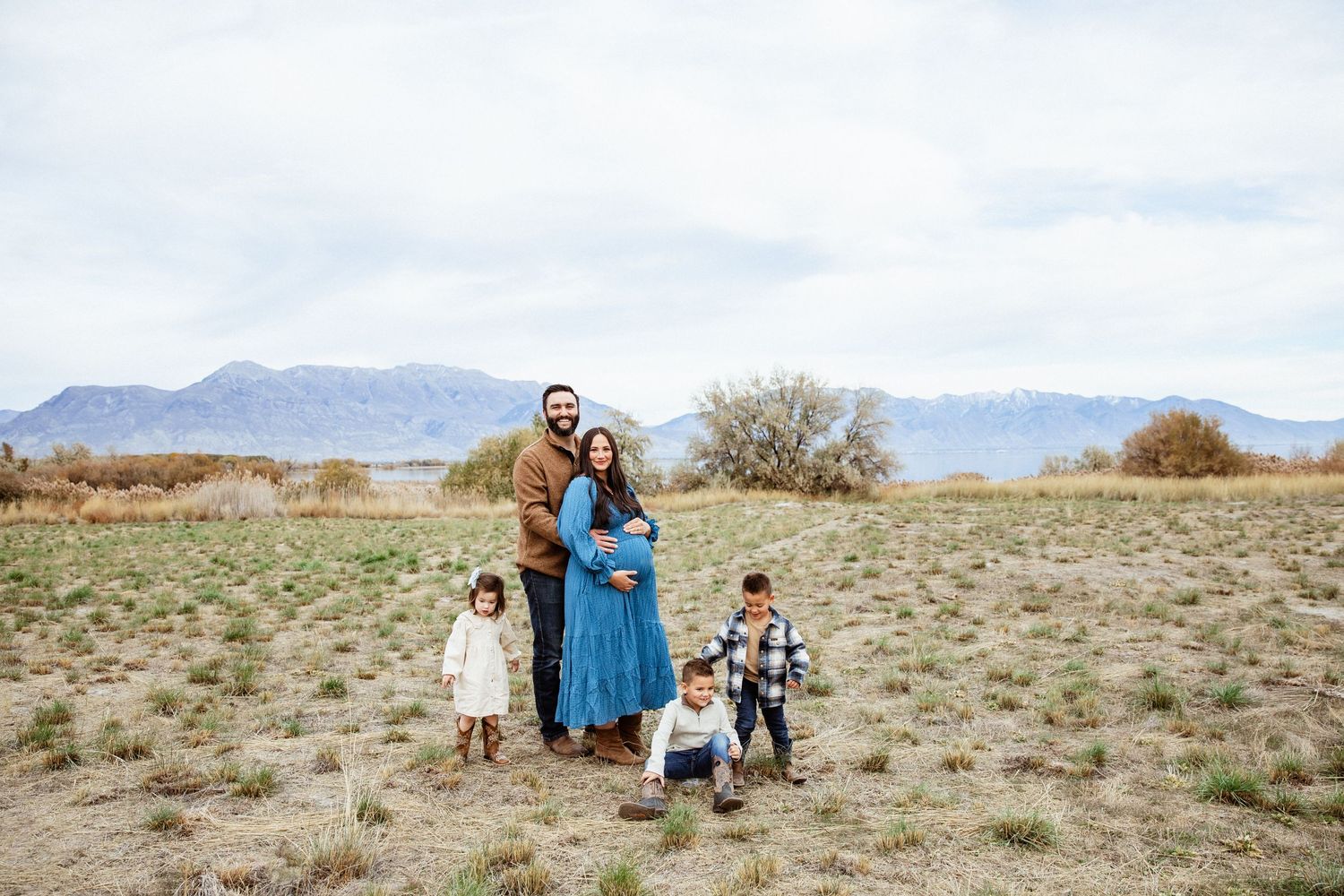 A family portrait in an open field with mountains and cloudy sky in the background.