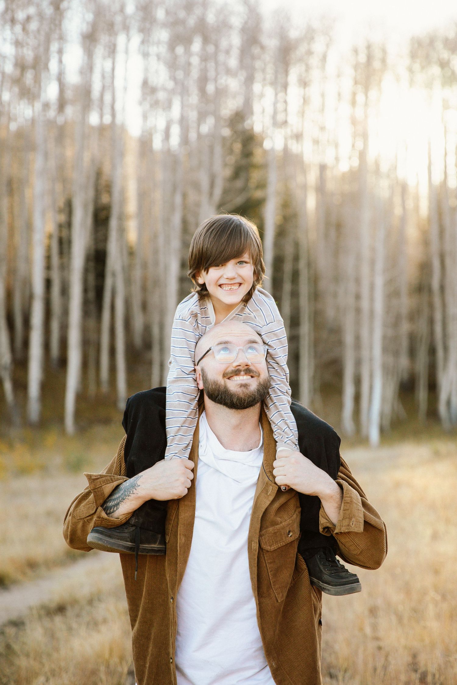 Joyful piggyback ride moment captured in a grove of white aspen trees during golden hour.