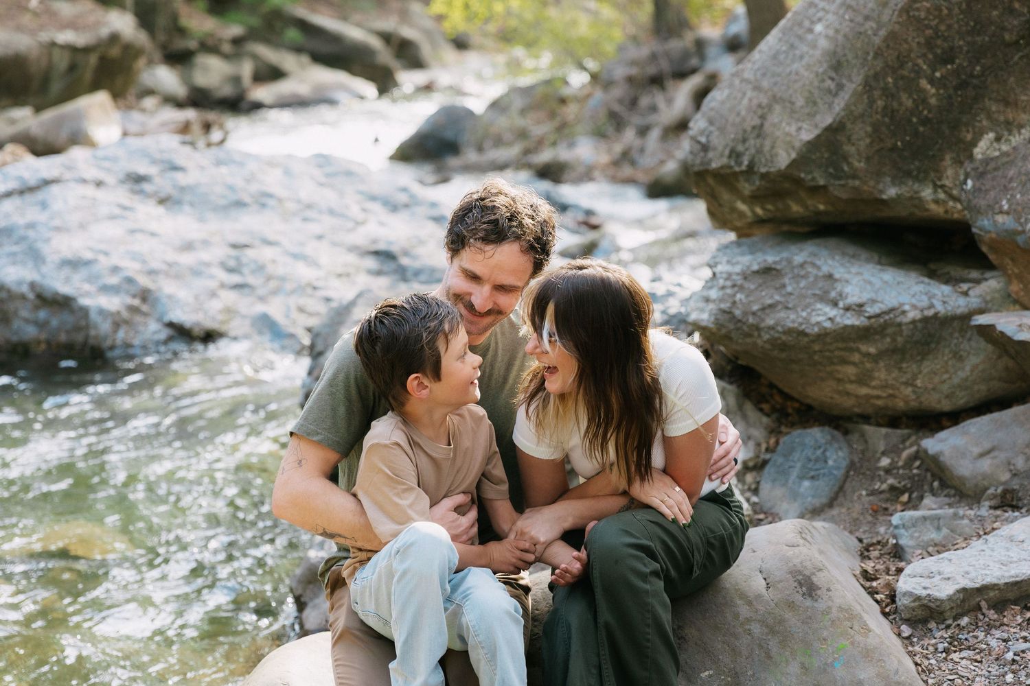 A couple shares an intimate moment while sitting together on rocky terrain near flowing water.