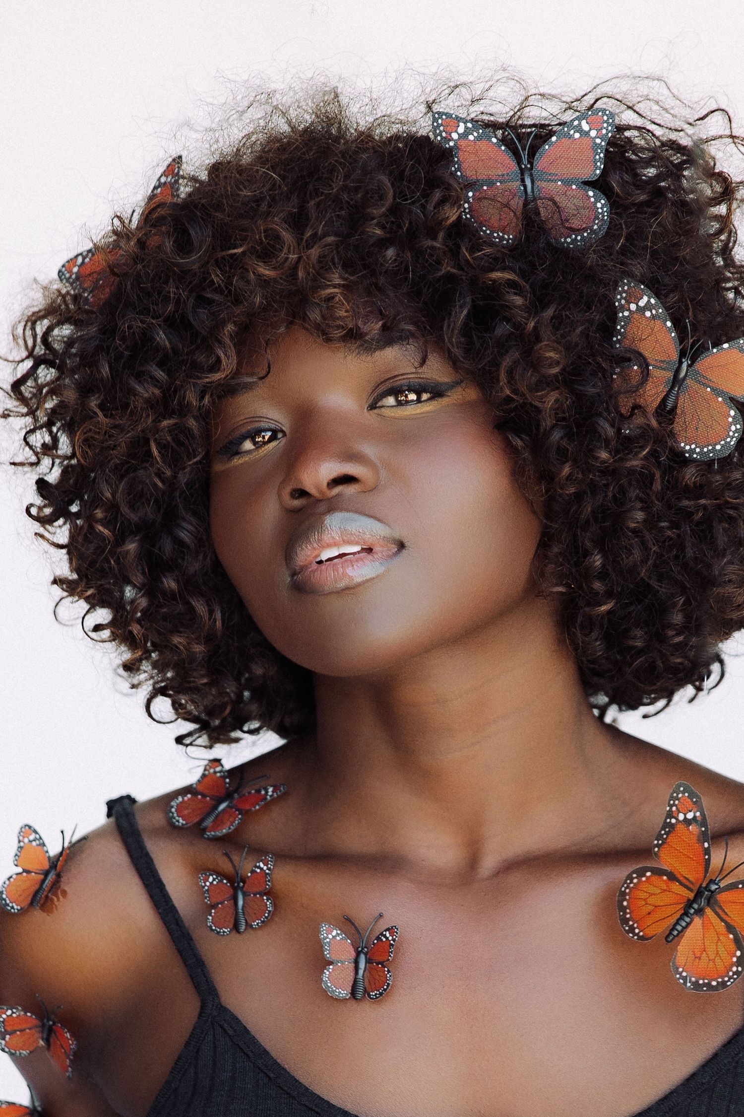 Artistic portrait with orange monarch butterflies decorating natural curly hair against white background.