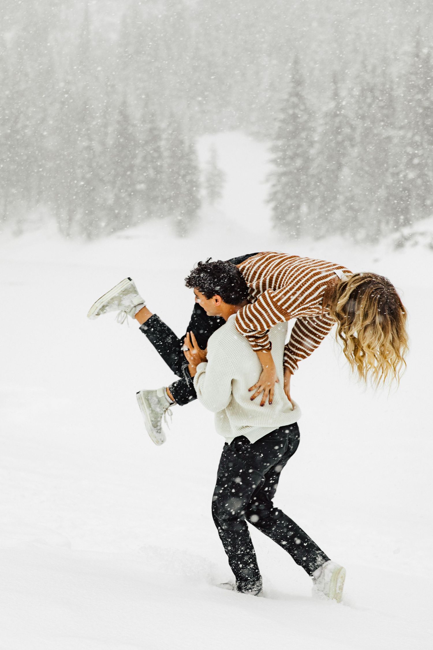 Playful couple having fun with a lift pose in the falling snow.