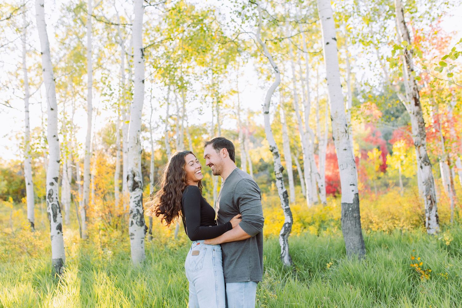 Couple walking hand in hand through aspen grove with golden fall foliage.