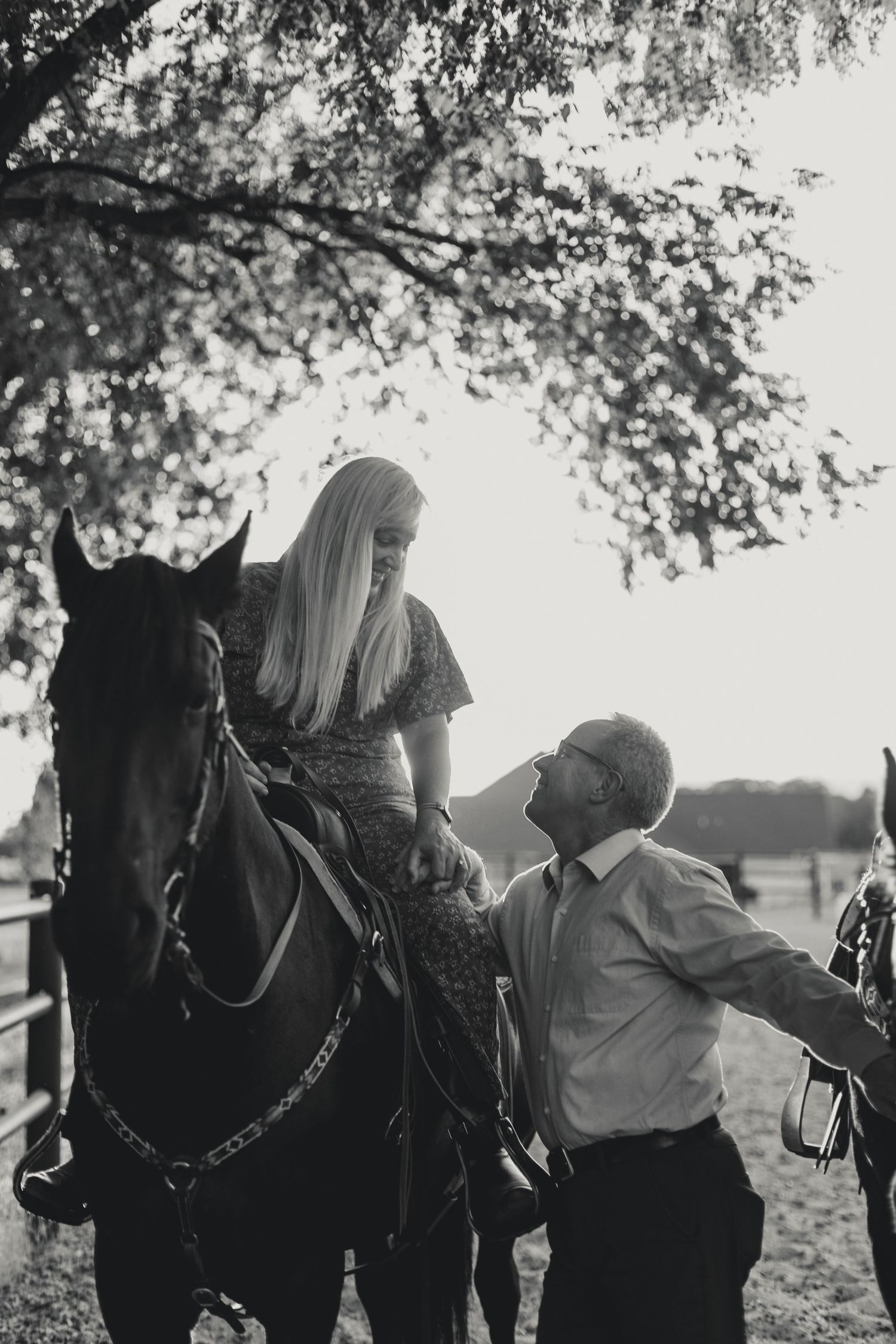A black and white photo of two people sharing a tender moment with a horse under a tree.
