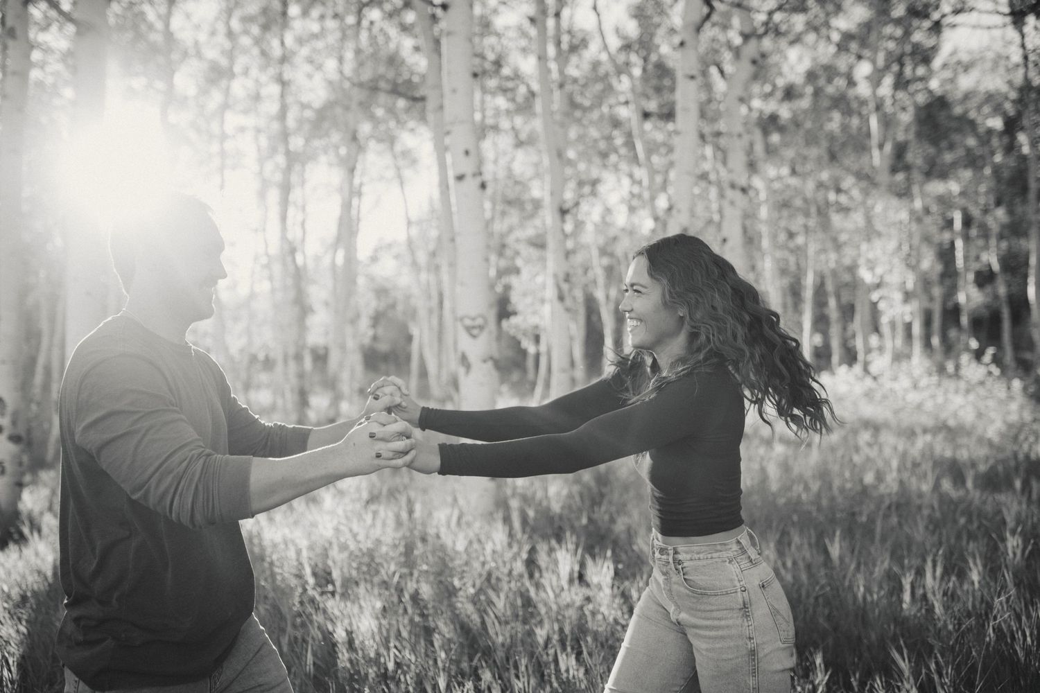 A playful black and white photo of a couple dancing in a sunlit forest.