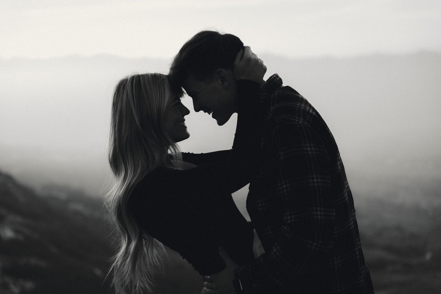 Romantic couple embraces in a scenic mountain landscape at sunset.