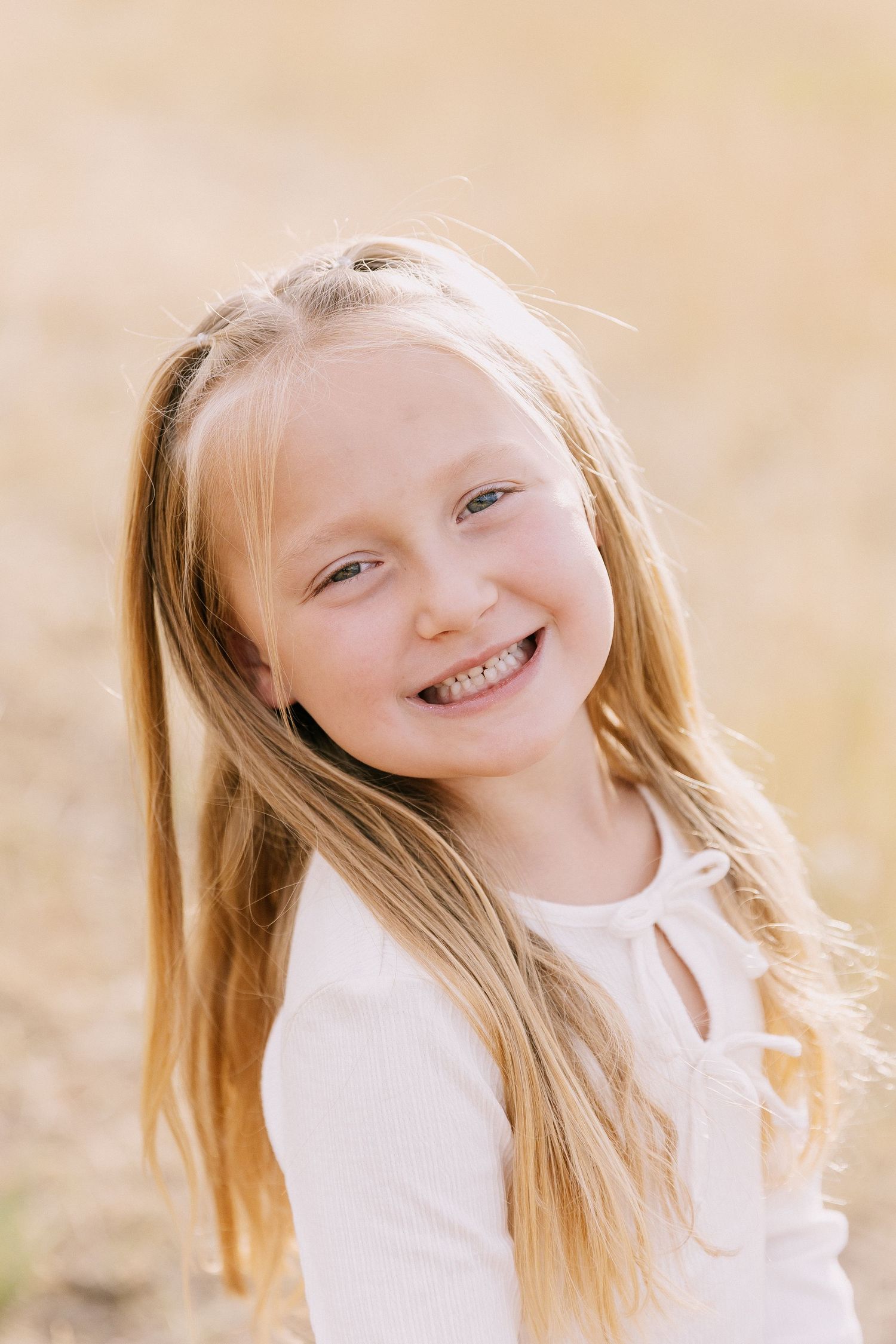 A joyful expression shines through with blonde hair and a white top against a soft, warm beige background.