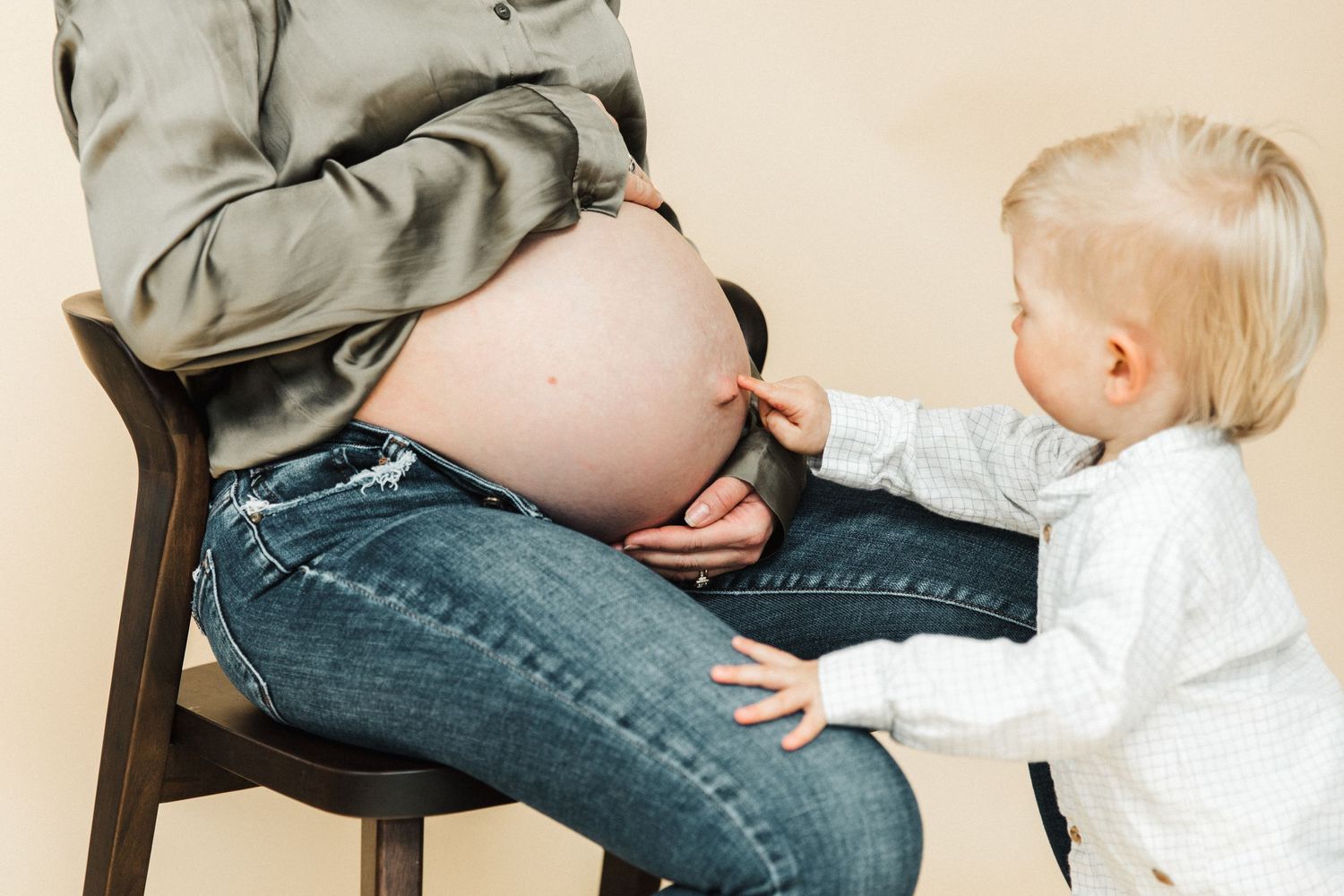 Toddler reaches out to touch mother's pregnant belly during photo shoot.