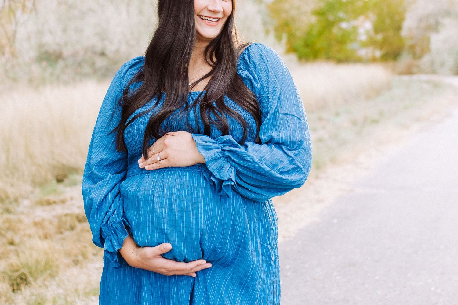 Expectant mother in bright blue dress poses outdoors during sunset photoshoot.