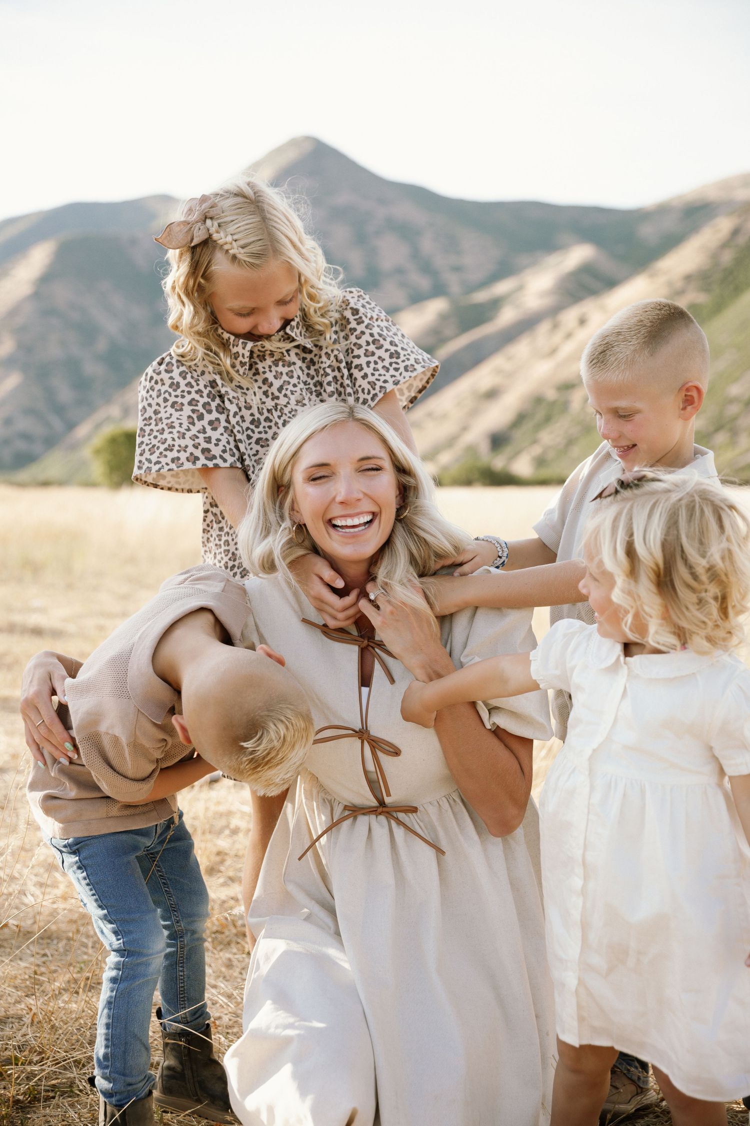 A series of candid family photos showing joyful moments and laughter in a golden field with mountains in the background.