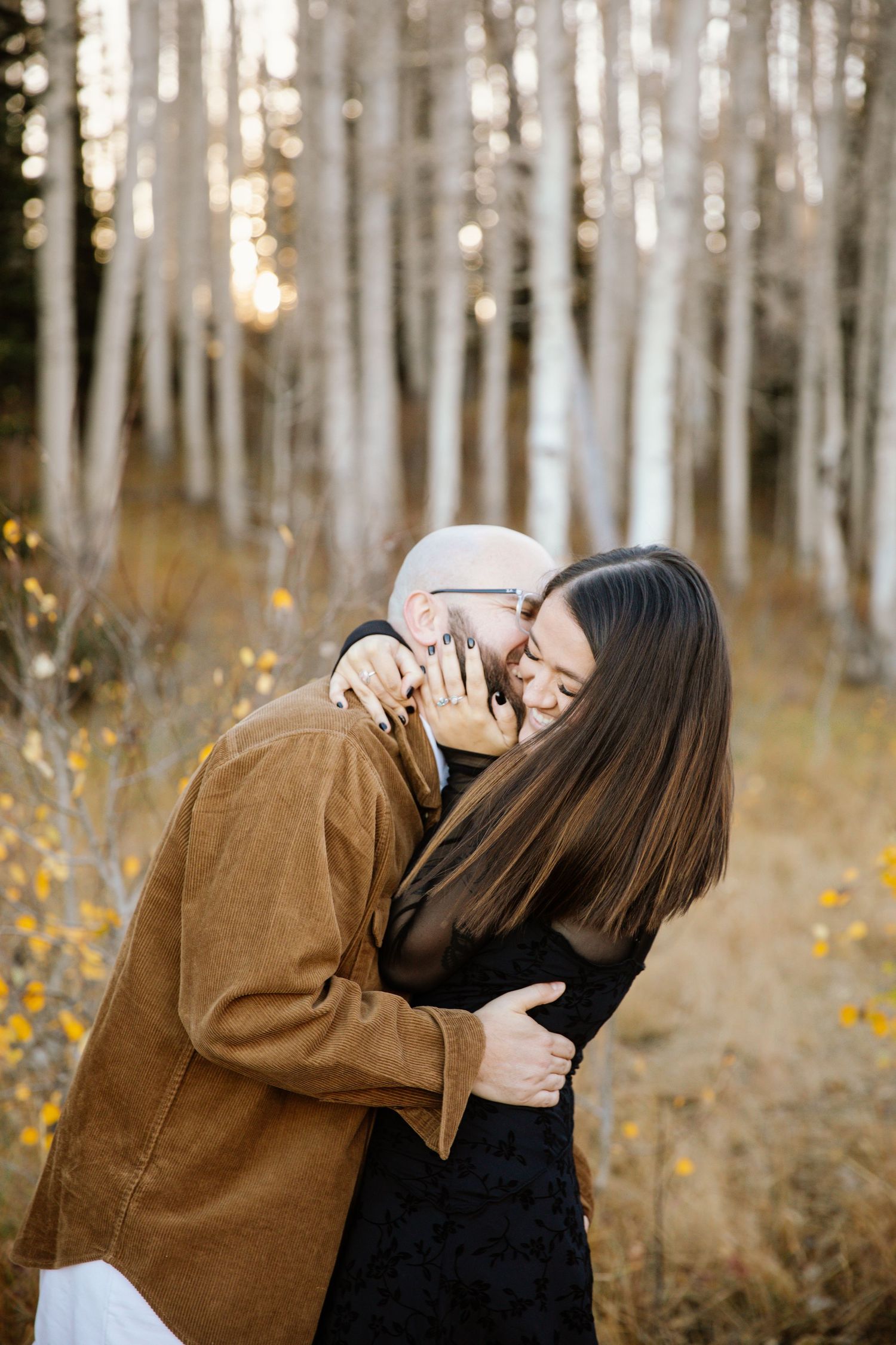 Couple embracing in an autumn aspen forest with golden sunlight filtering through the trees.