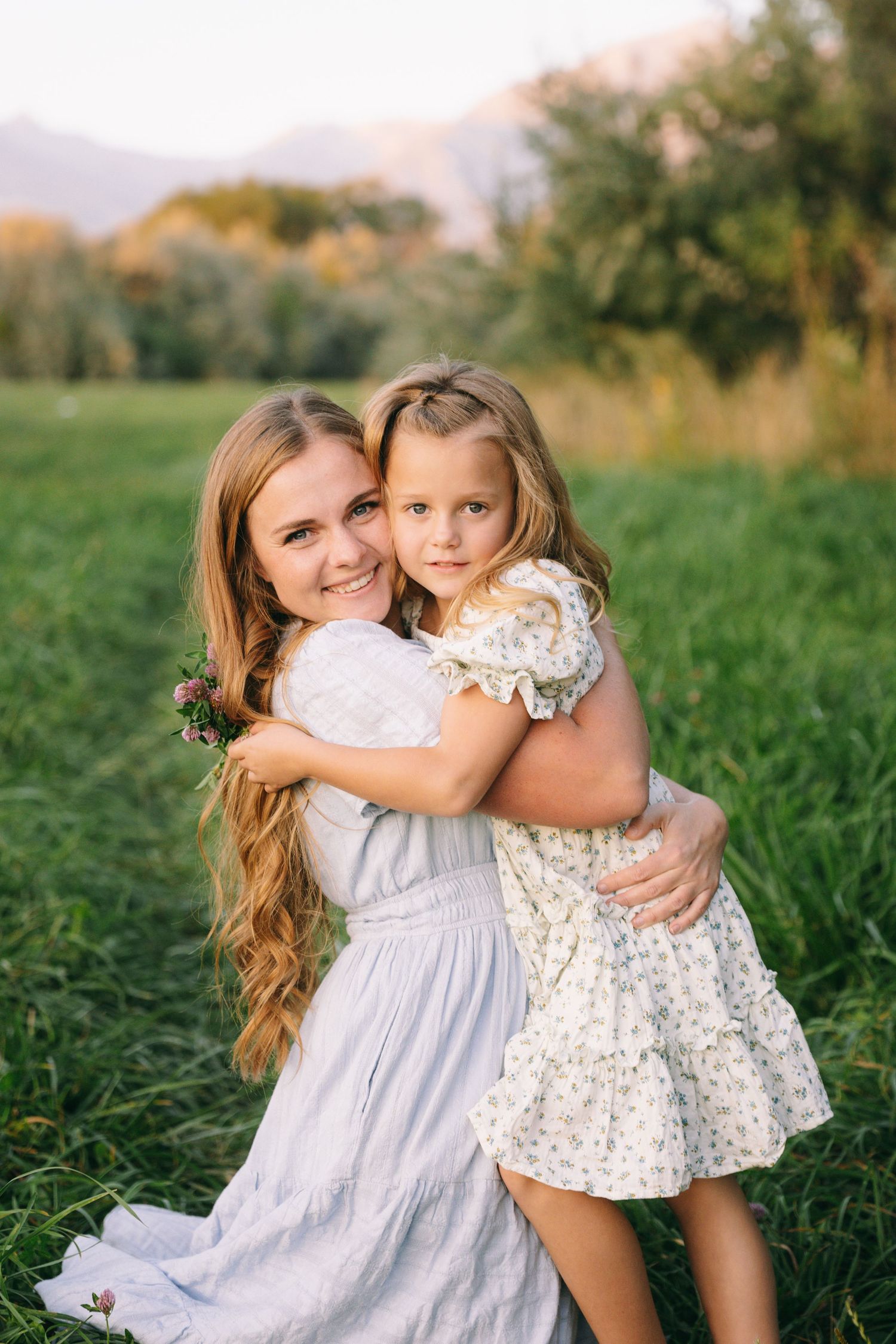 A tender outdoor photoshoot in a grassy field shows a sweet embrace against a warm sunset backdrop.