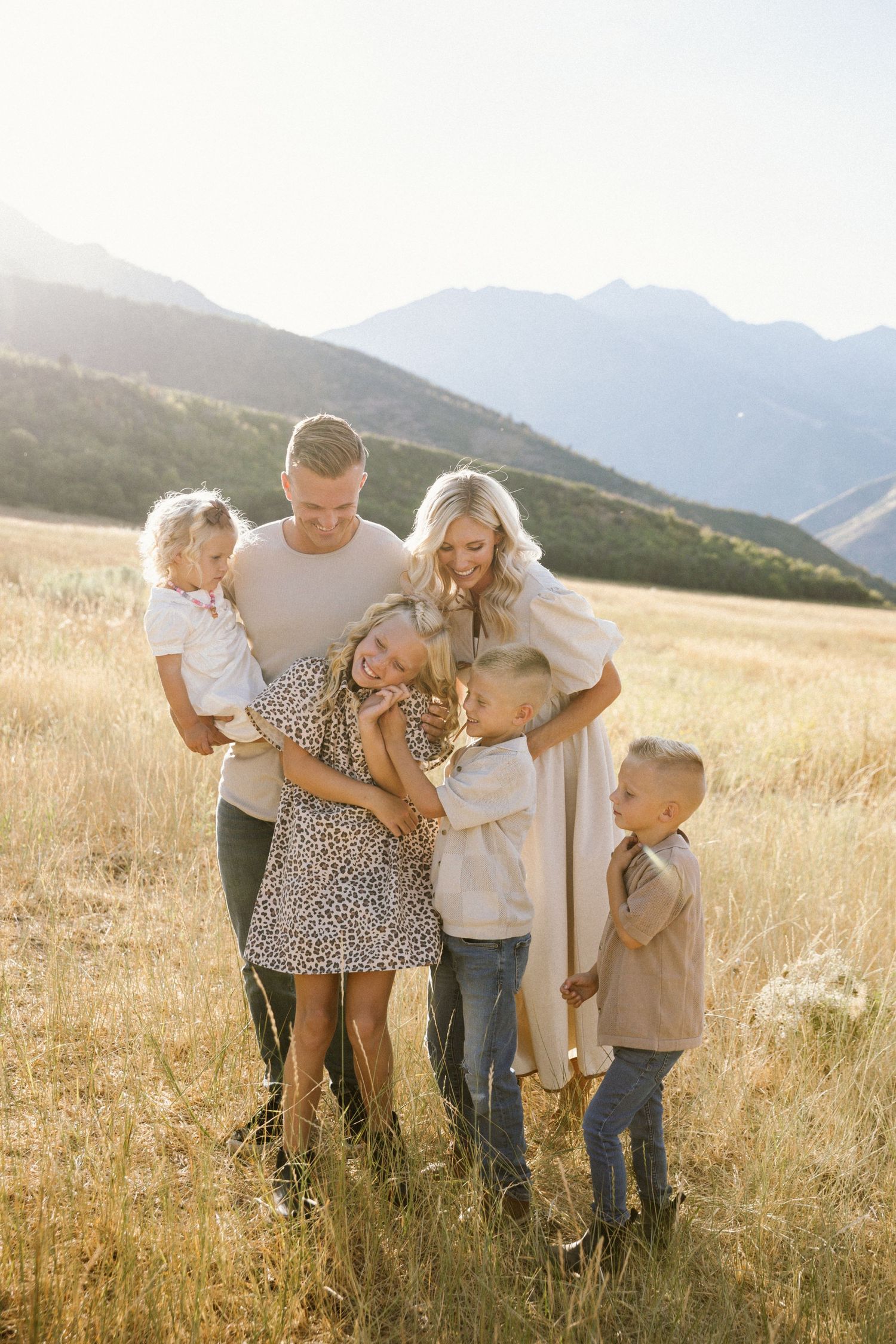 A family shares joyful moments together in a golden field with mountain views during sunset.