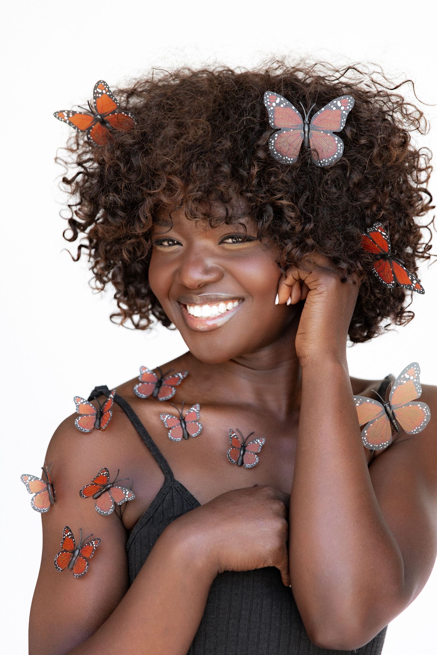 Natural beauty portrait with orange butterflies and curly hair against white backdrop.