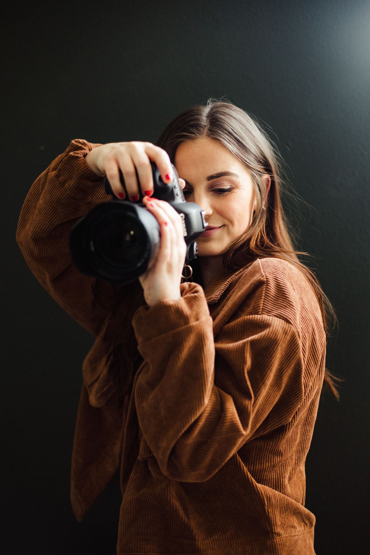 Person in brown sweater taking artistic self-portraits against dark background.