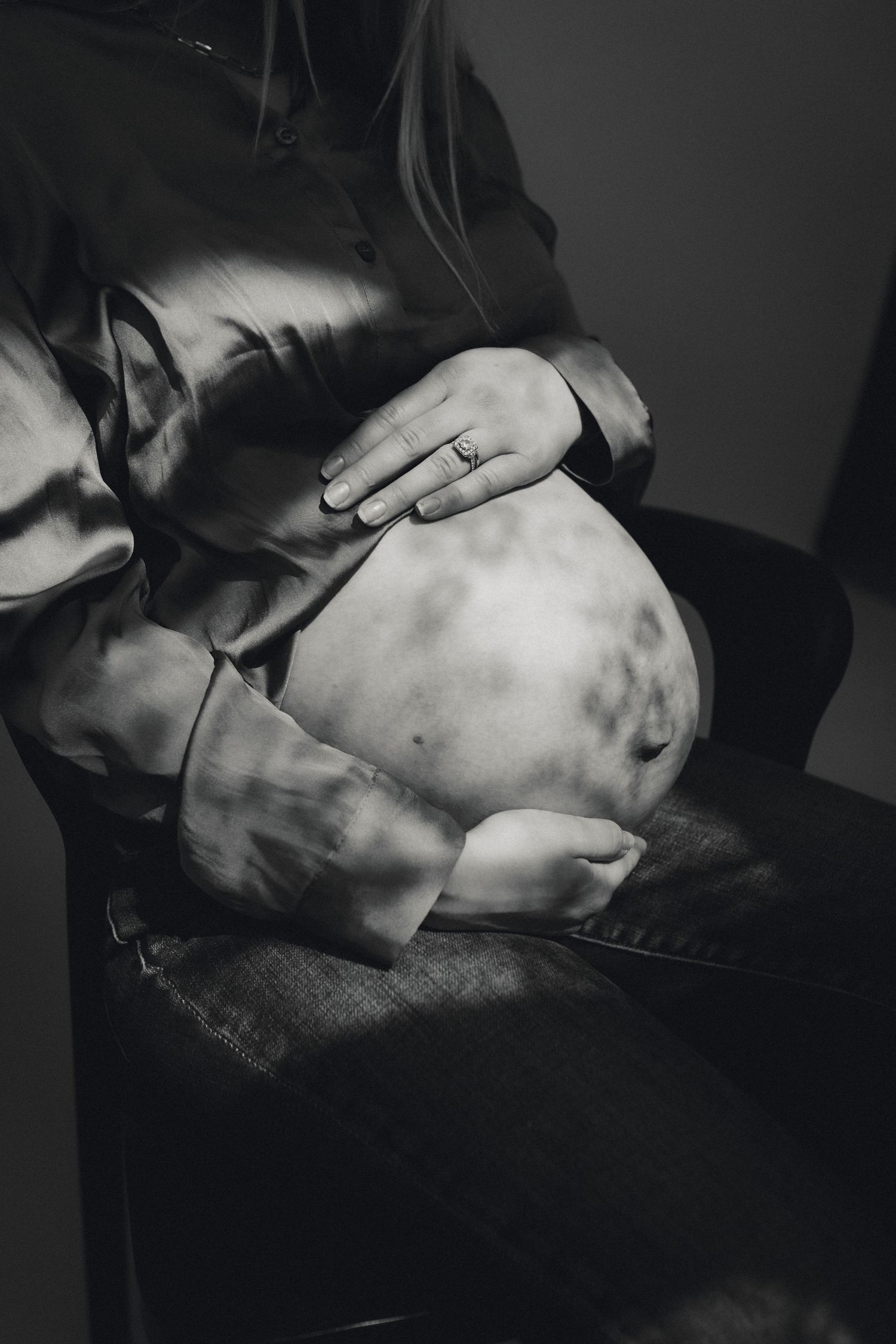 Black and white close-up of hands cradling pregnant belly in silk shirt.