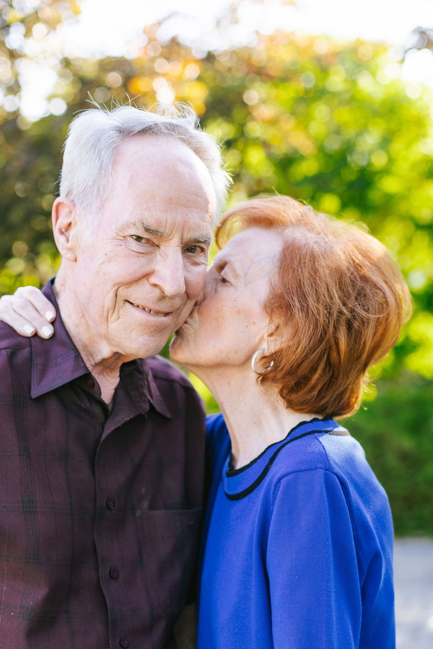 A couple shares a tender moment in a sunny garden setting with green foliage.