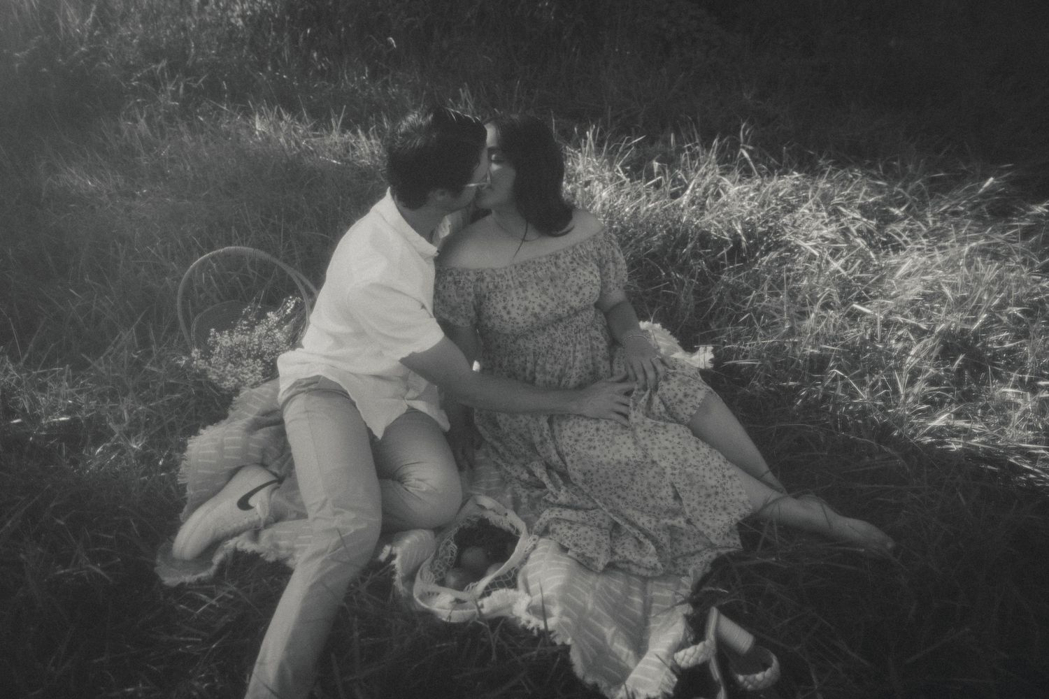 Black and white photo of a couple relaxing in a meadow during sunset.