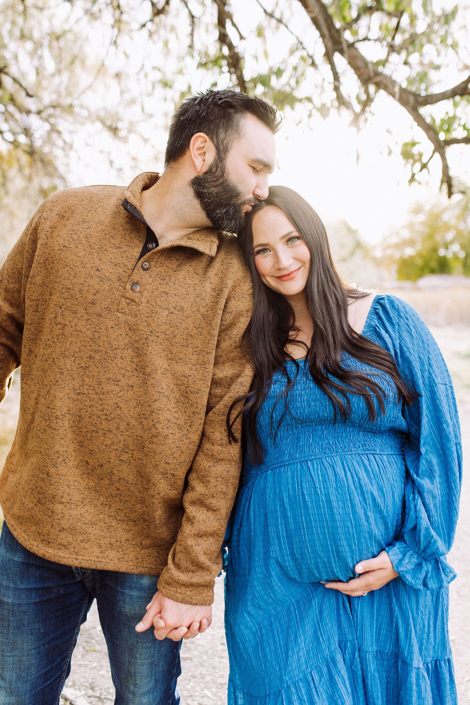 Intimate maternity photo showing couple holding hands outdoors with natural lighting.