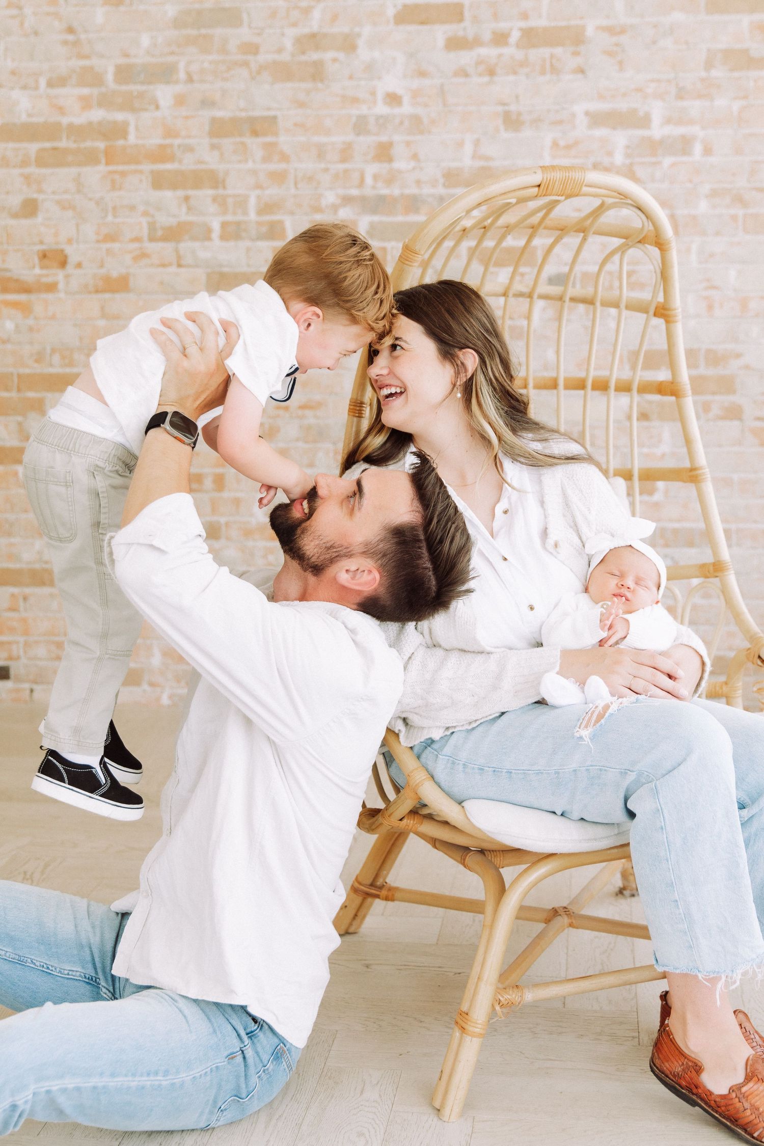 Playful family poses on rattan chair against exposed brick wall.