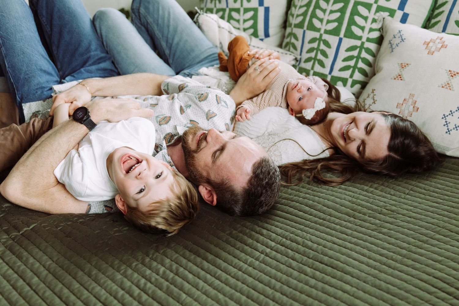 Group lying together on a green patterned couch sharing a joyful moment.