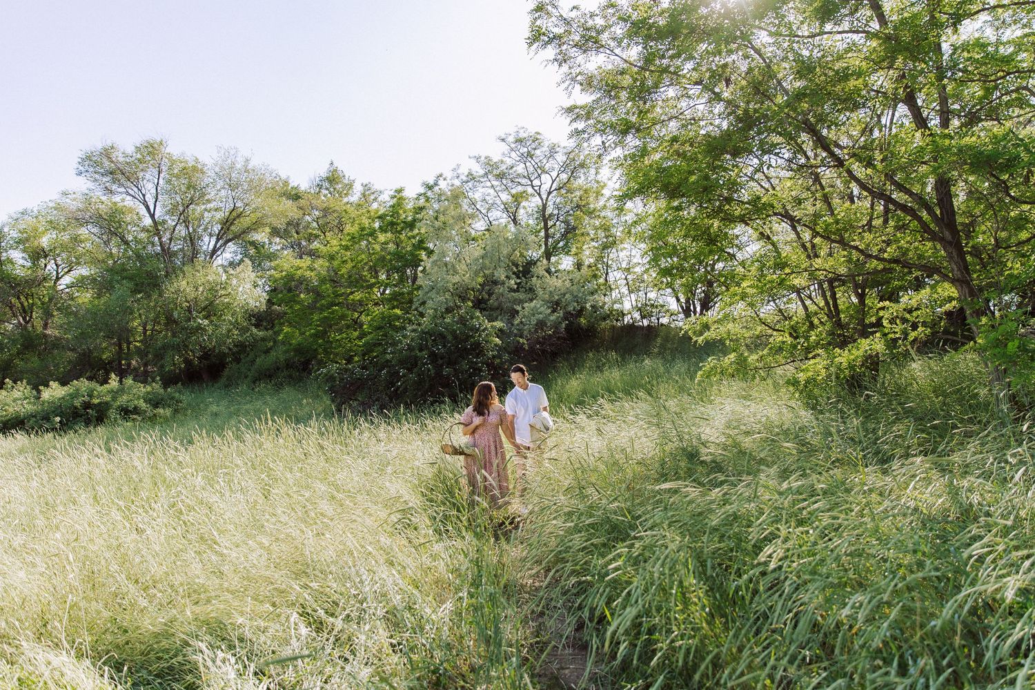 Couple walking through tall summer grass in a sunlit natural meadow.